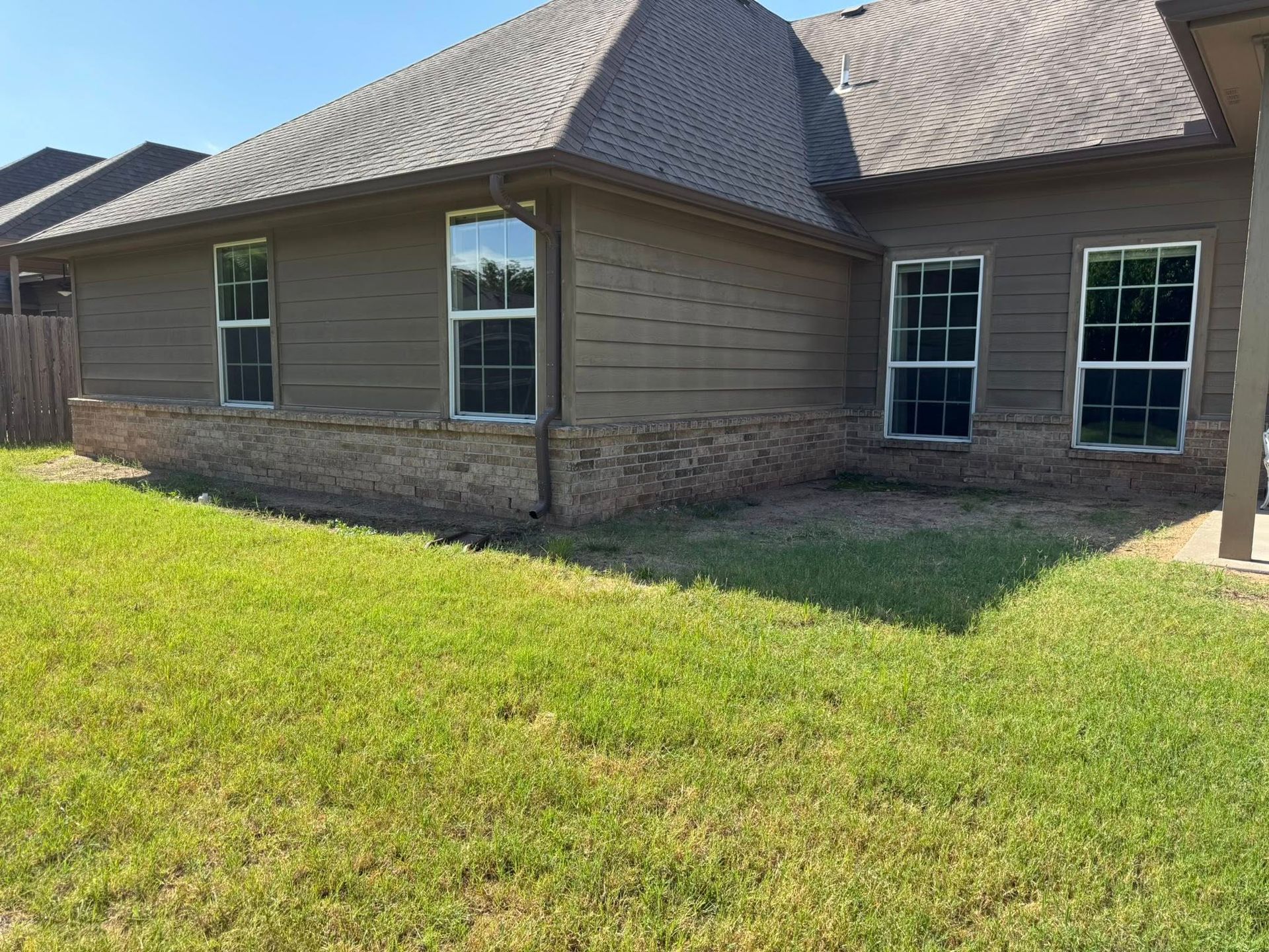 Brown house with a brick base and windows, surrounded by green grass.