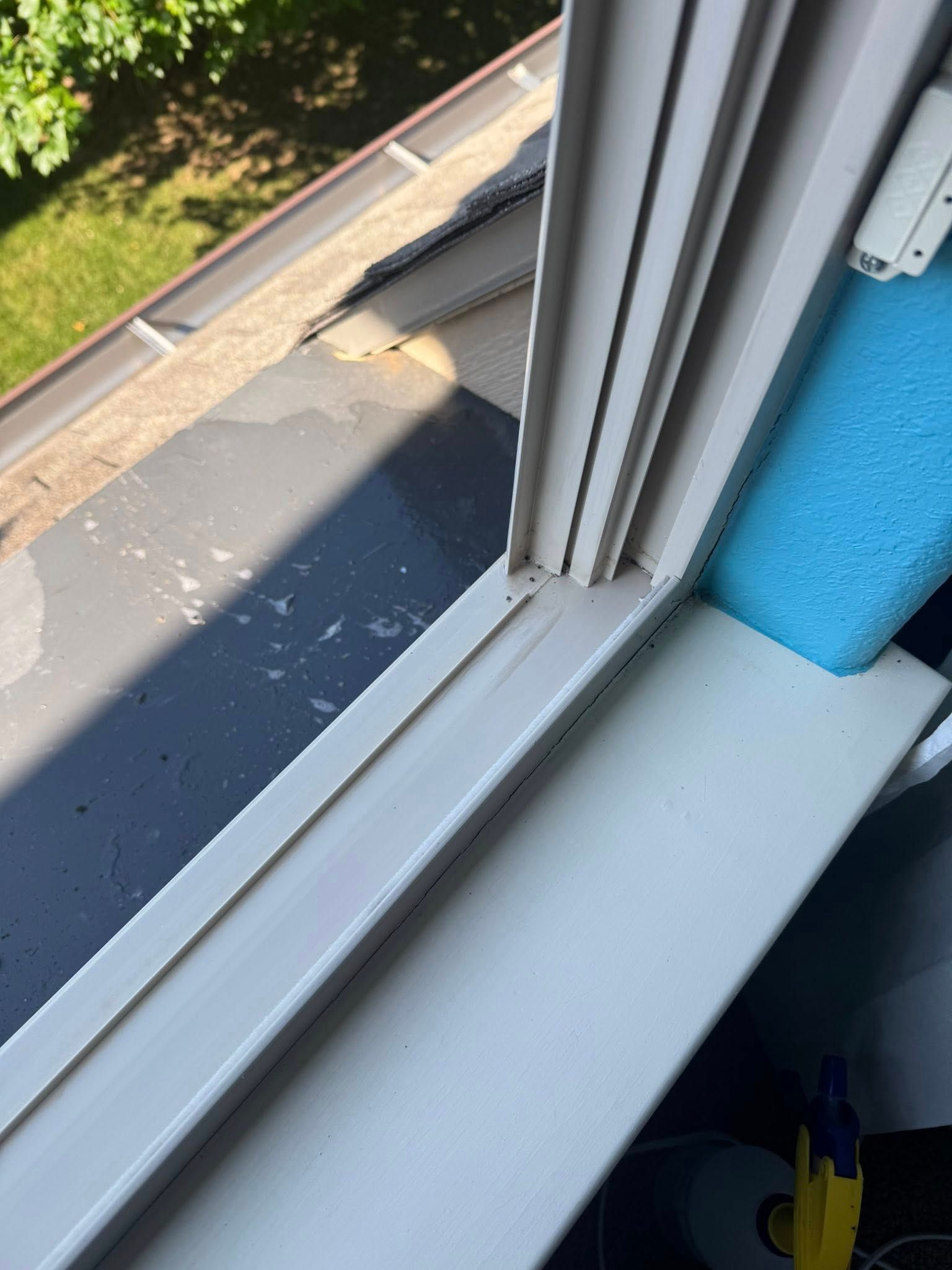 White window frame against a dark surface, with a blue foam block. Sunlight on a rooftop.