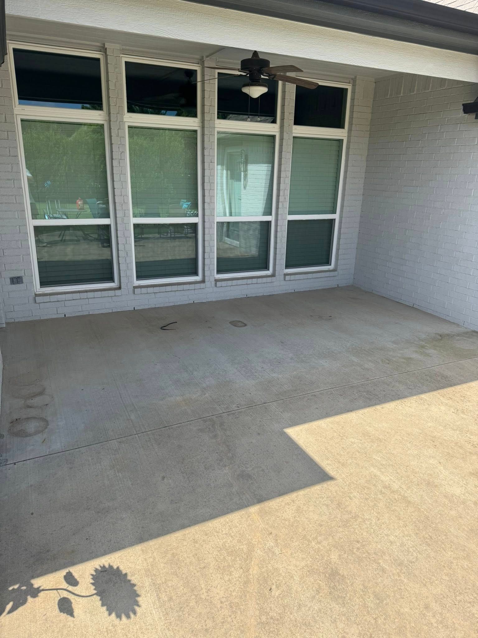 Covered outdoor patio with concrete floor, brick walls, and tall windows.