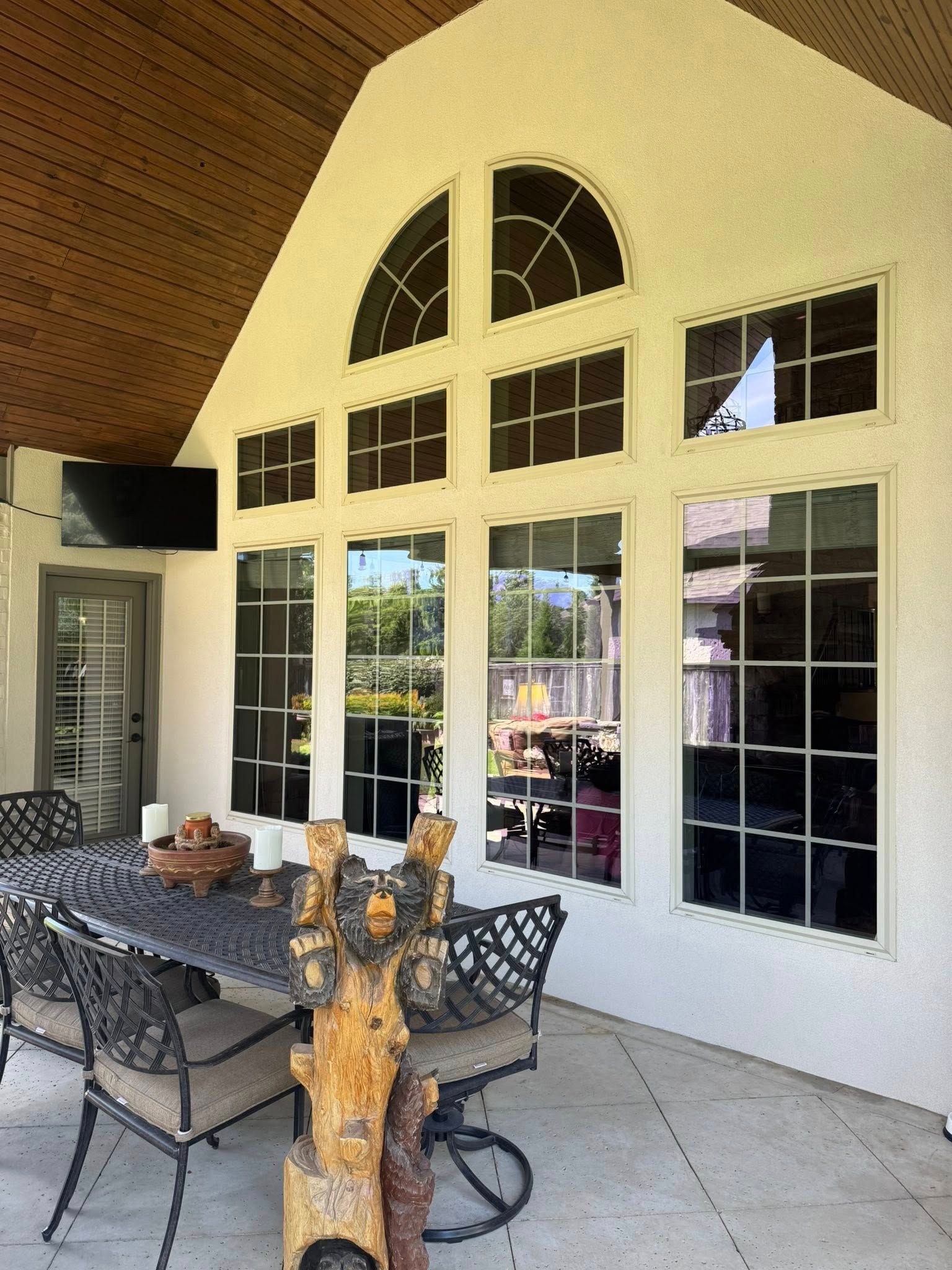 Patio with dark-tinted windows, a table, and chairs; neutral-colored exterior with a partially covered roof.