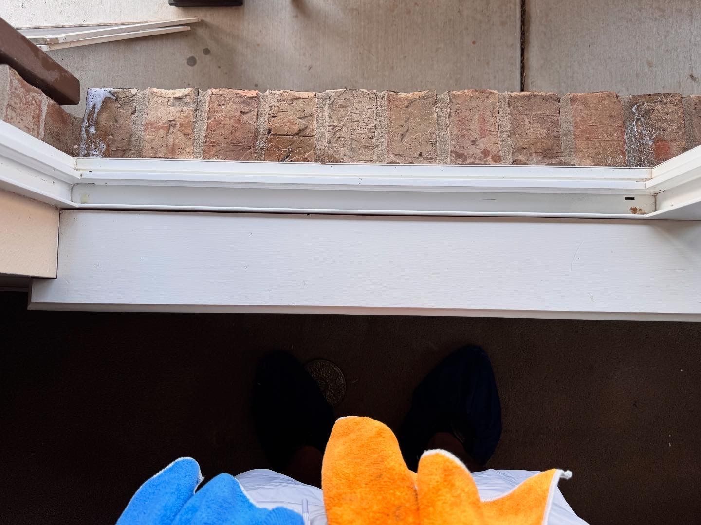 Person's view looking down at feet, blue and orange fuzzy objects, brick wall, and door frame.