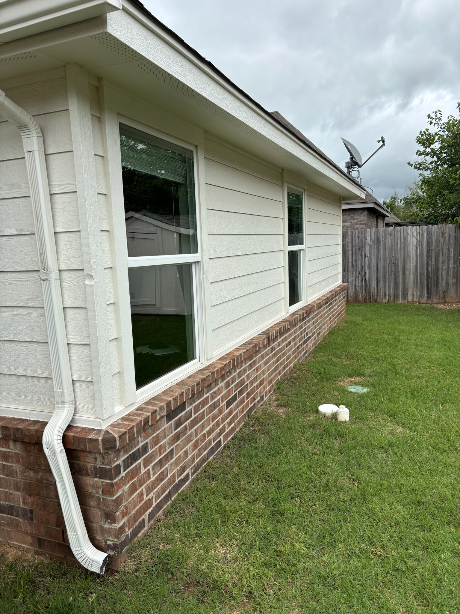Exterior of a house with white siding above a brick base, two windows, and a green lawn.