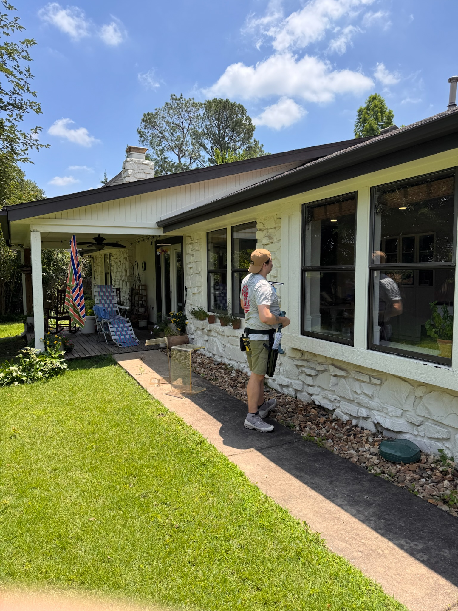 A person cleaning windows of a white brick house on a sunny day.