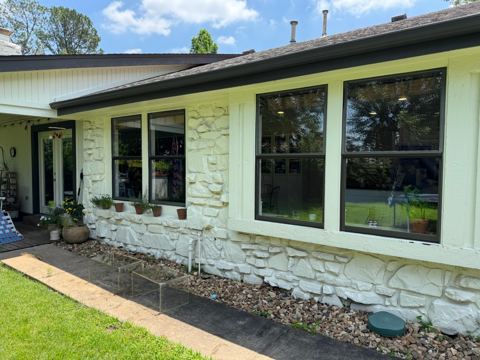 White stone house with black-framed windows, dark roof, and green lawn.