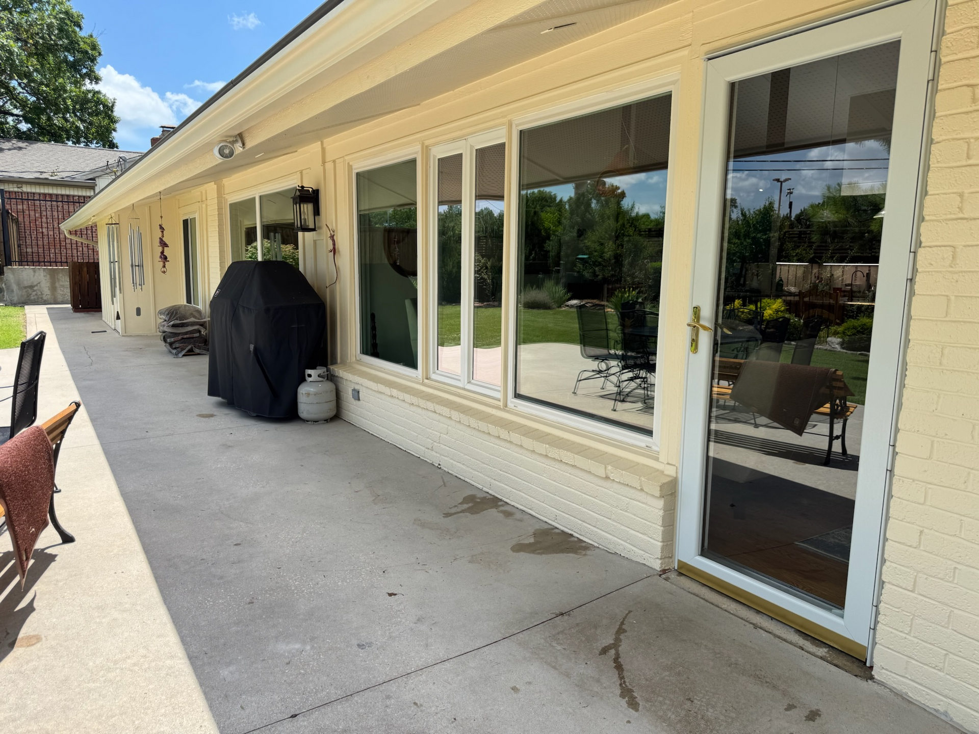 Exterior view of a house with a concrete patio, windows, and a door, with a grill and propane tank visible.