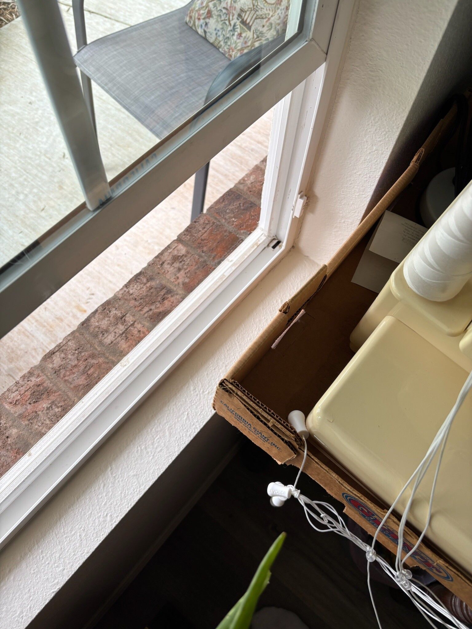 Window with white frame, brick exterior. Cardboard box with items sits in window sill.