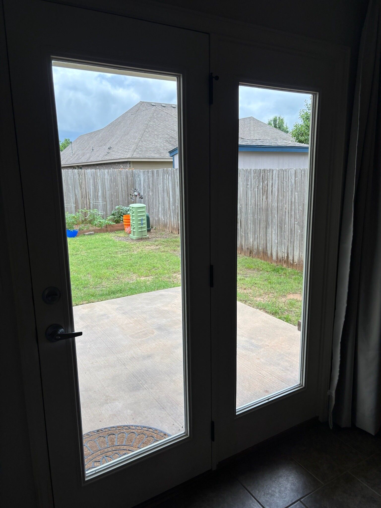 Two glass doors open to a backyard with a lawn, fence, and cloudy sky.