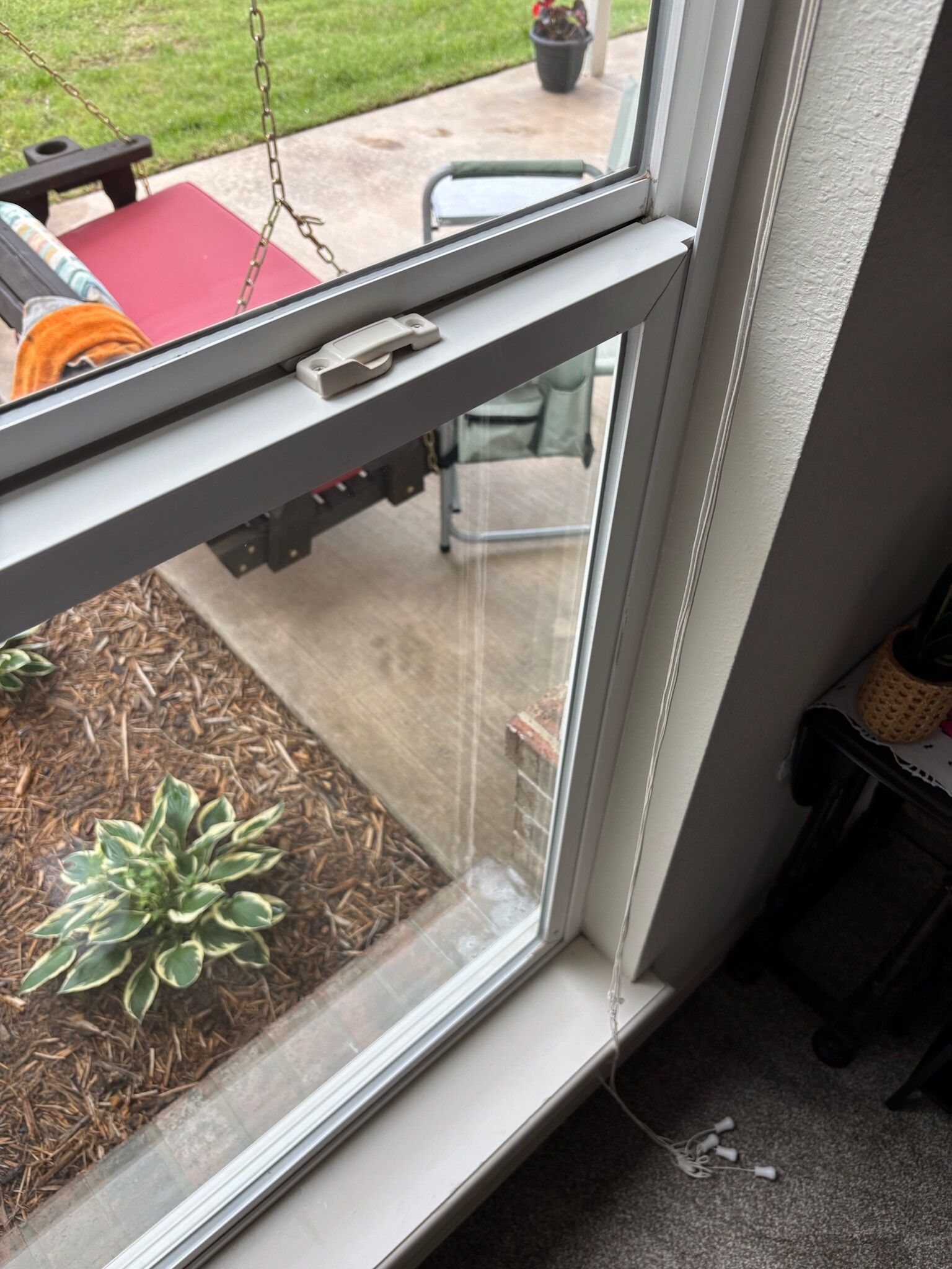 Open white window with a view of a patio and garden, metal lock on top frame.