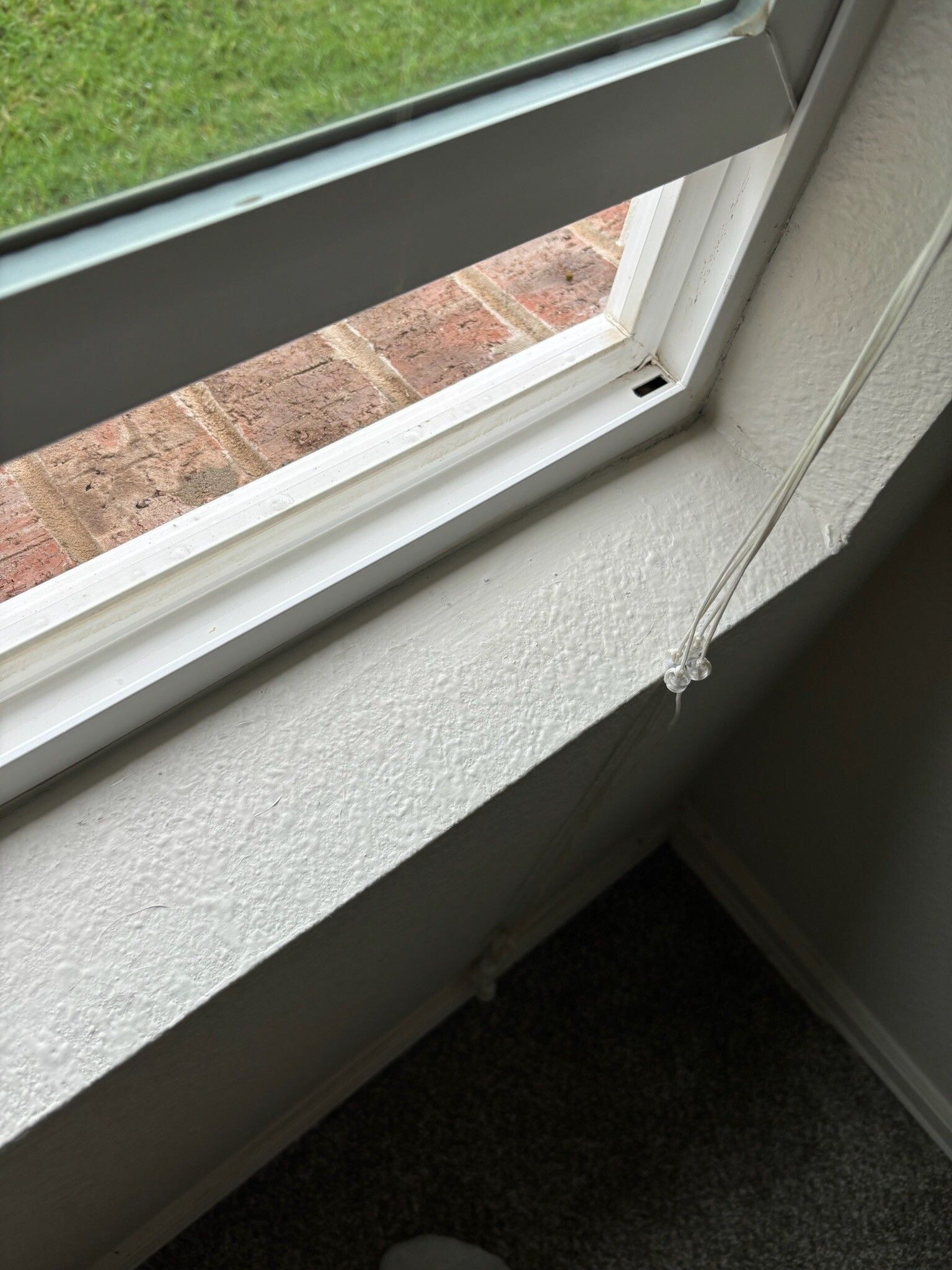 A partially open white skylight with a textured white wall and a hanging cord.