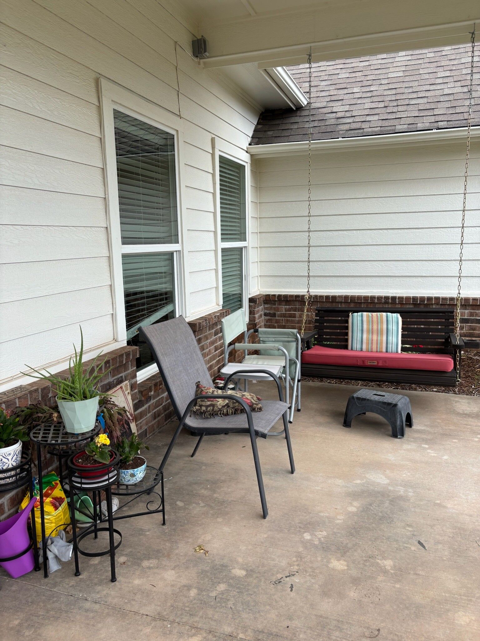 Porch with a swing, chairs, and potted plants.