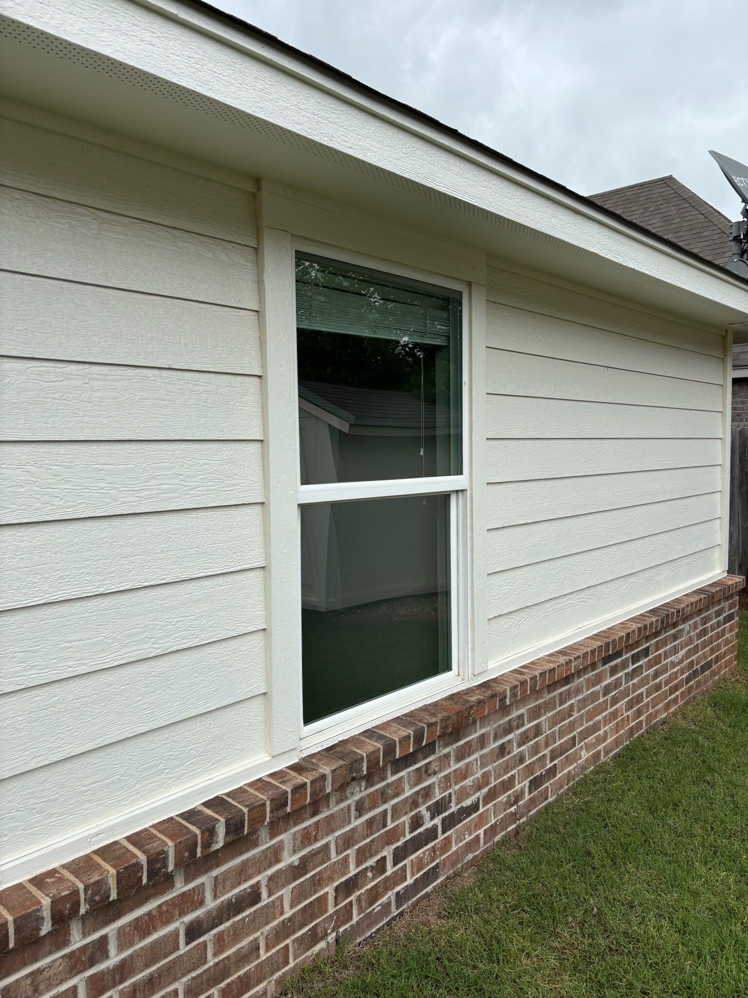 Exterior view of a house with white siding, a brick base, and a white-framed window.