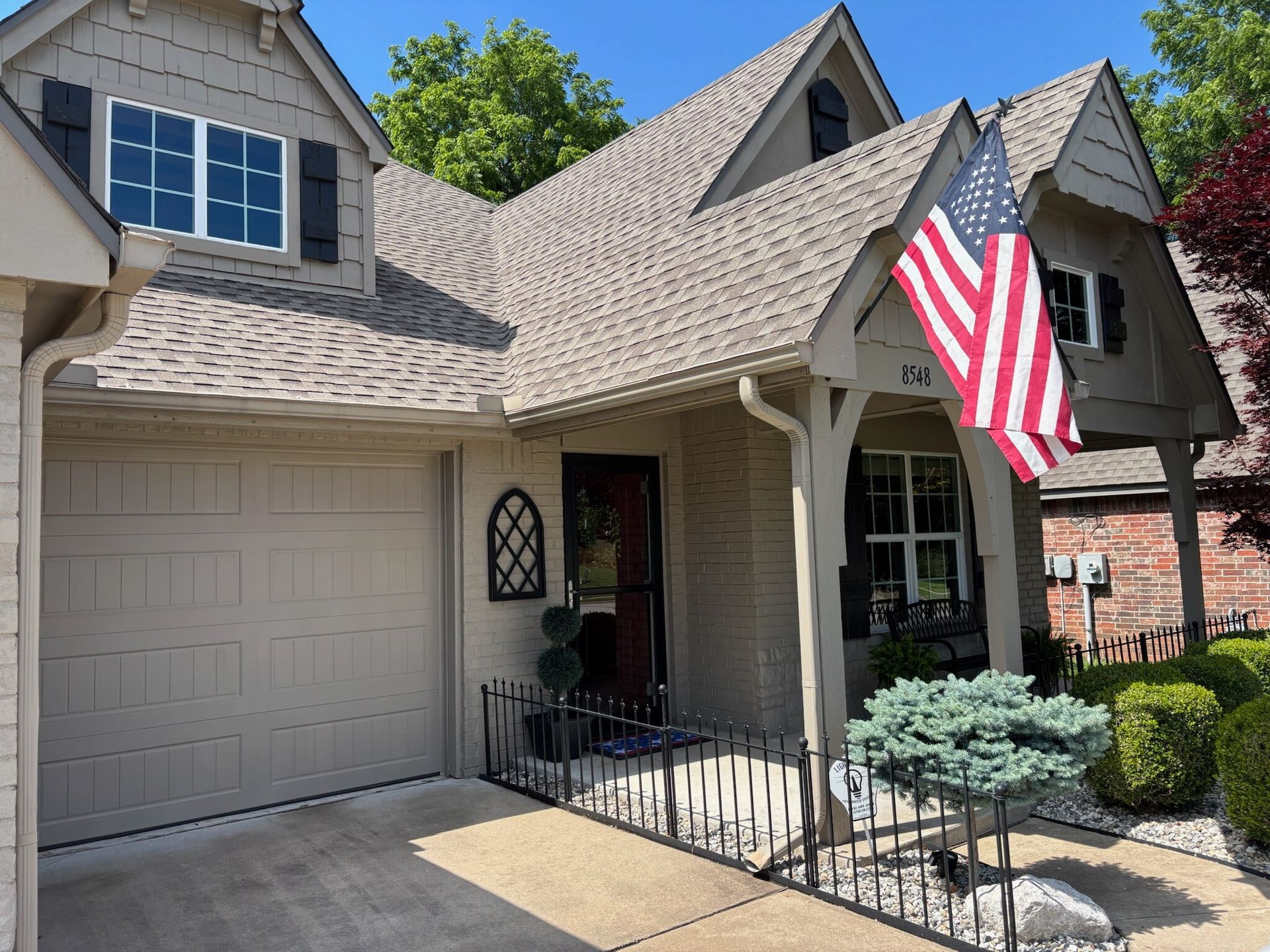 Tan house with an American flag, arched entry, garage, and walkway with metal railing.