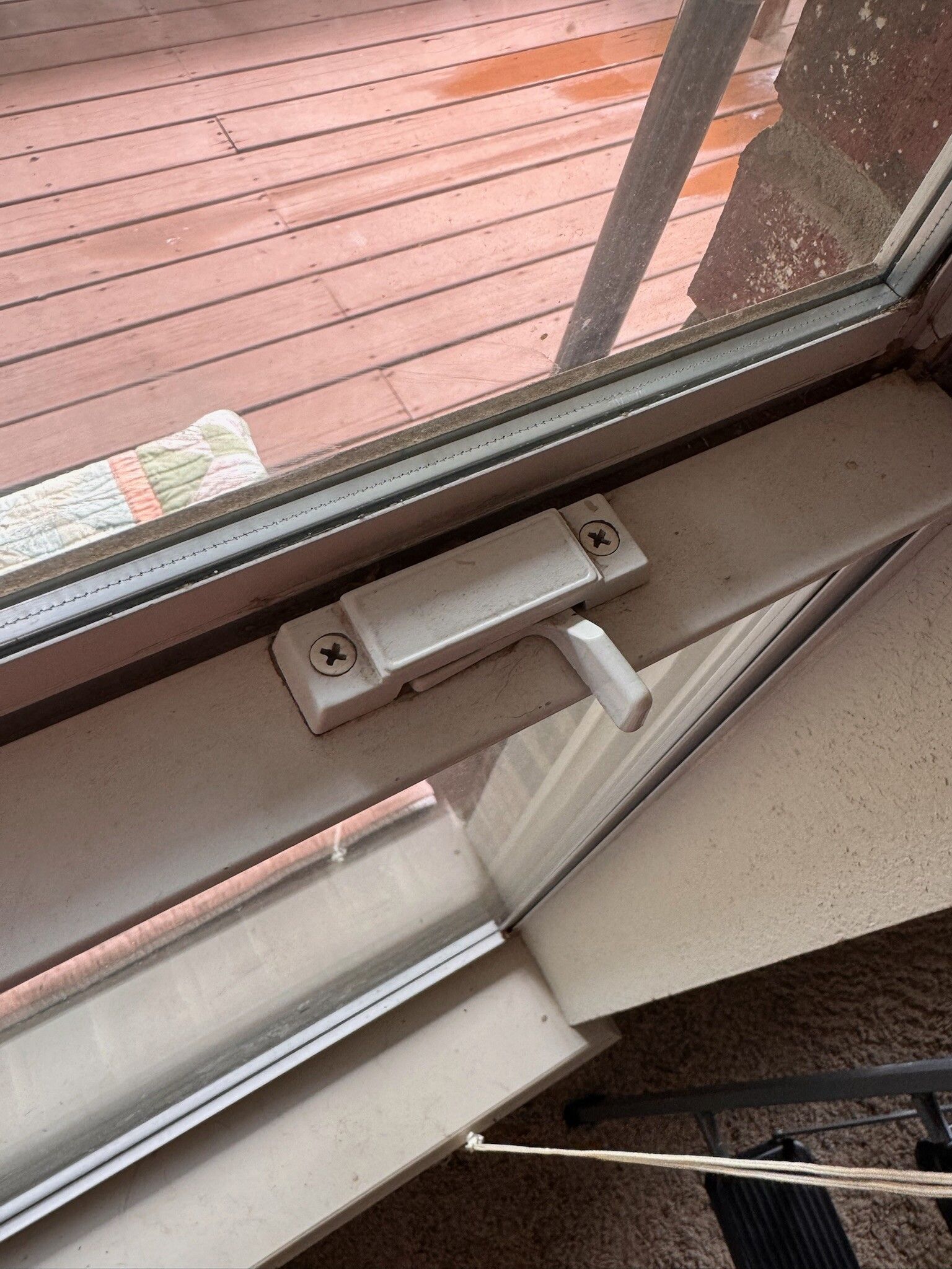White window latch with lever and screws on a window frame, near a wooden deck.