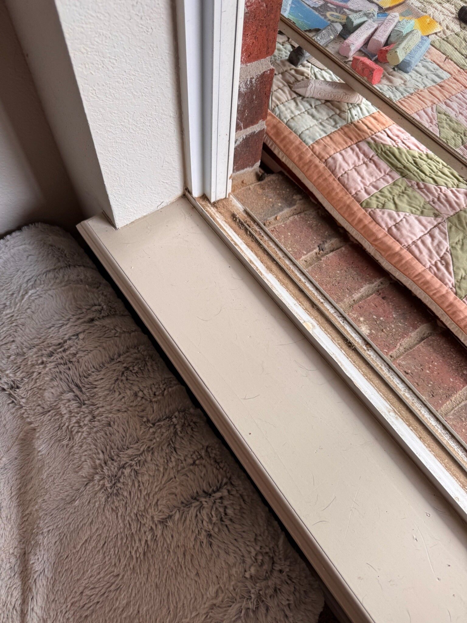 Close-up of a window ledge with painted trim and a brick exterior visible. A rug is on the left.