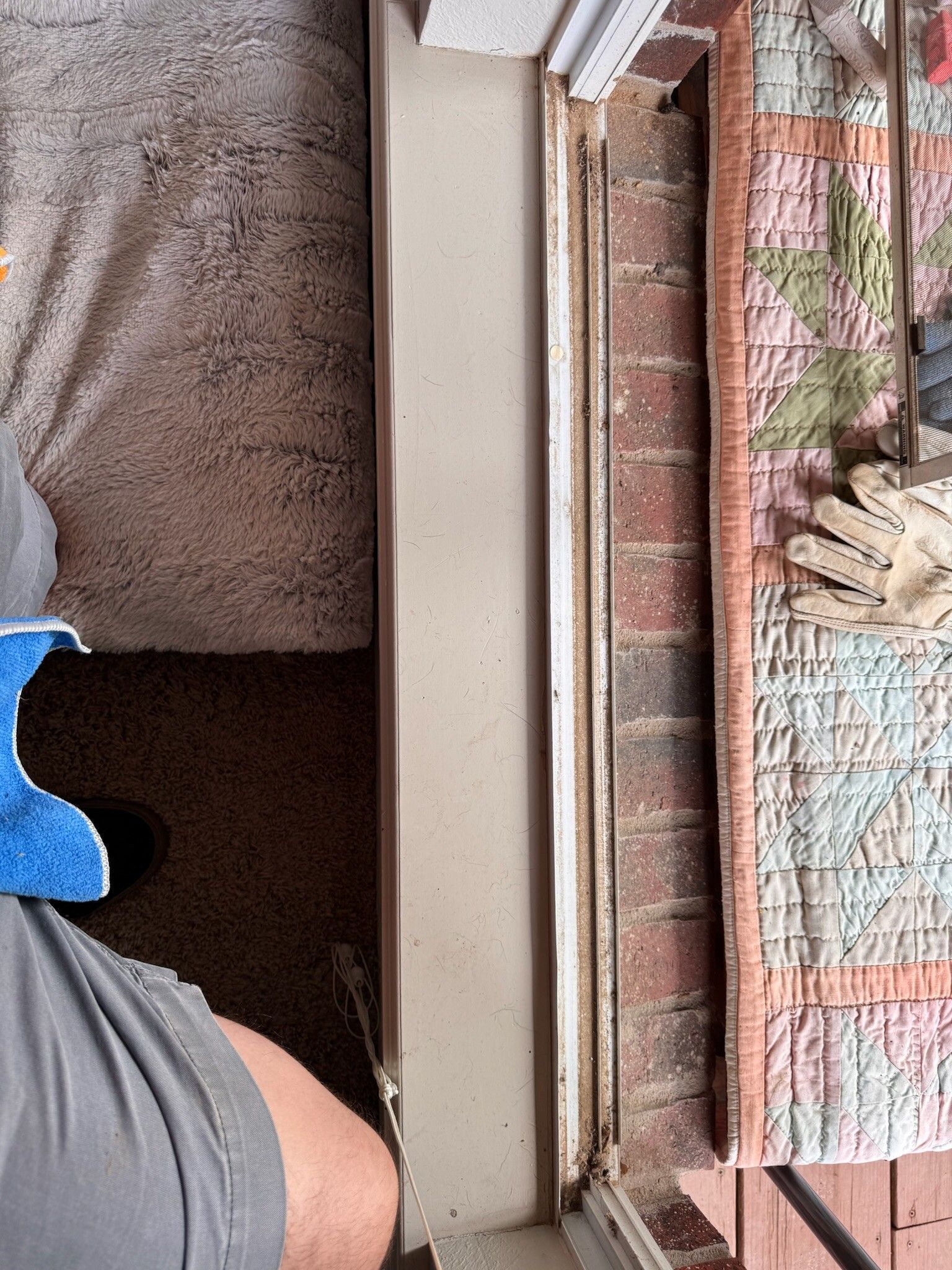 A person cleaning a window frame next to a brick wall and a decorative mat.