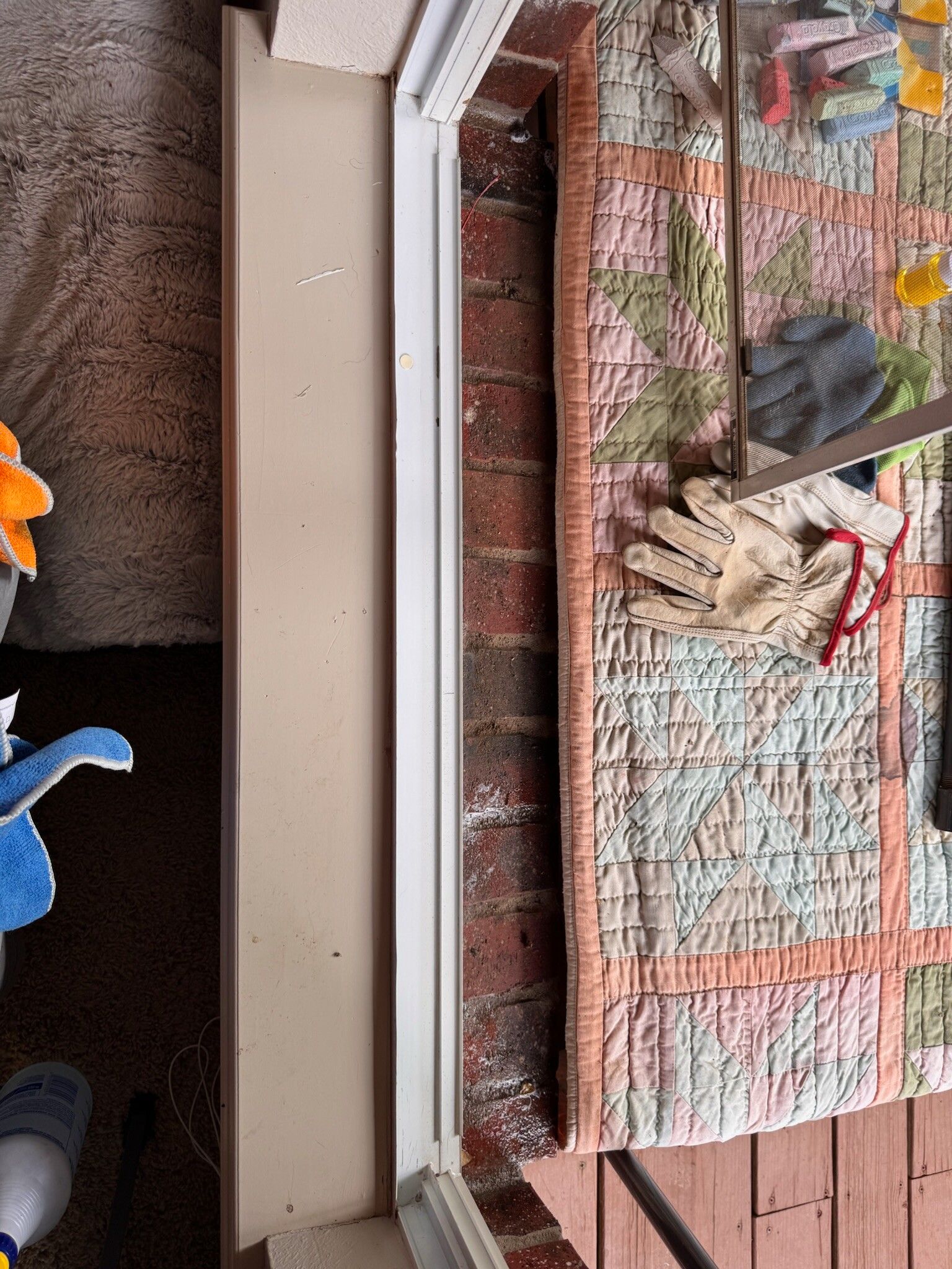 Side view of a window frame and exposed brick. Gloves and a quilt are on a surface visible through the window.