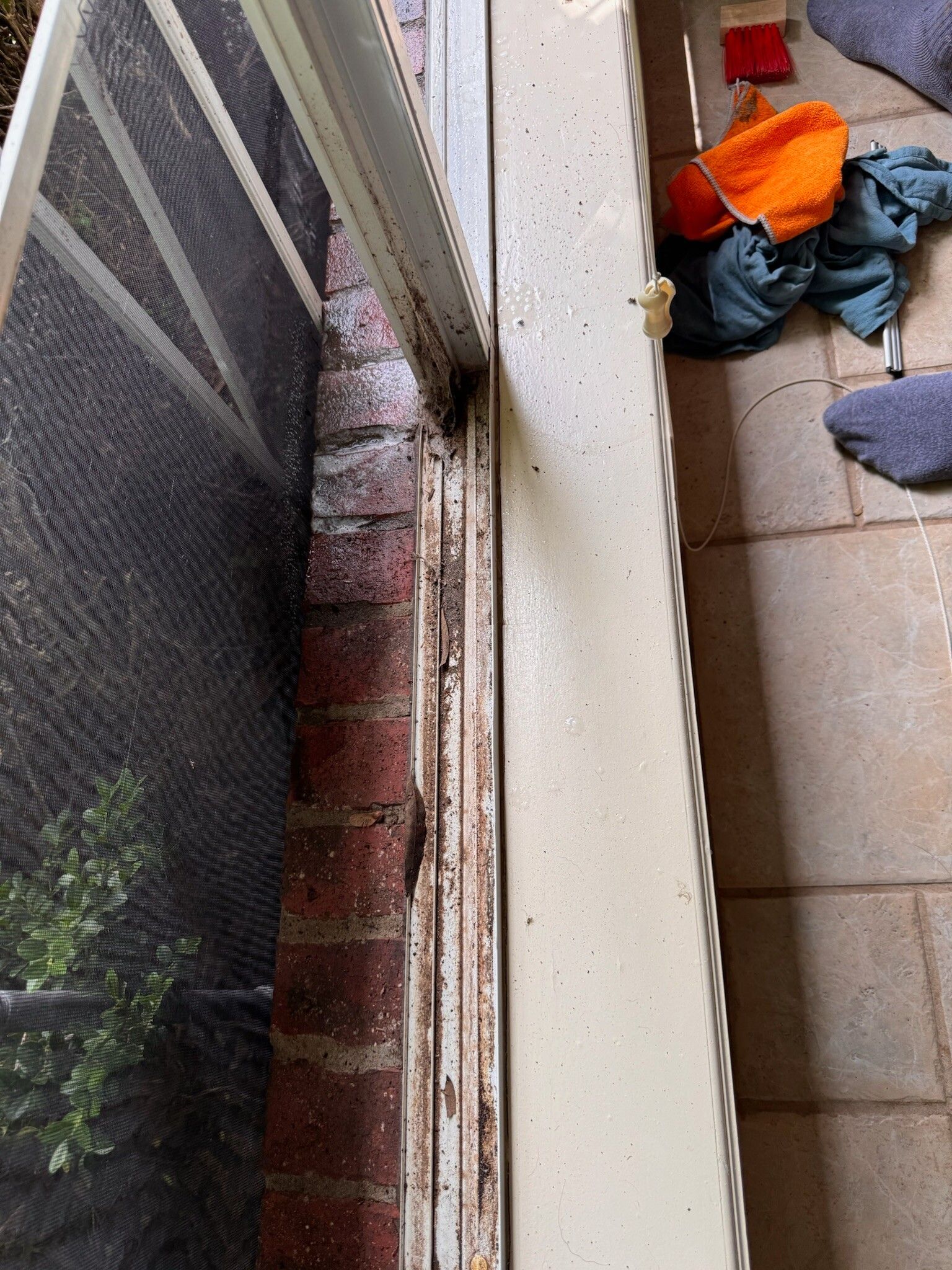 Window frame next to brick wall, with a screen and a dirty, dusty track.
