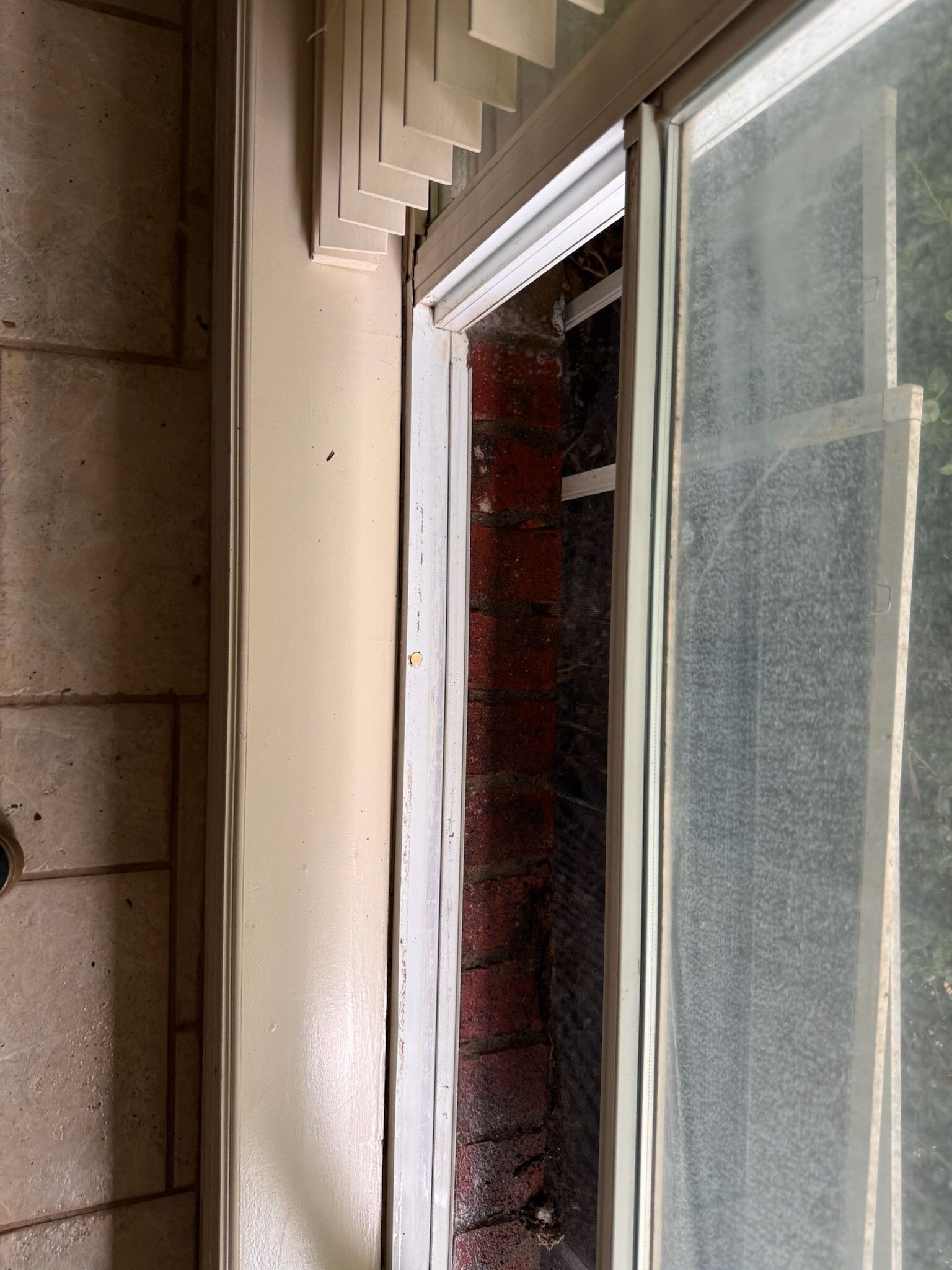 Close-up of a window frame with a venetian blind. Brick wall is visible through the window.