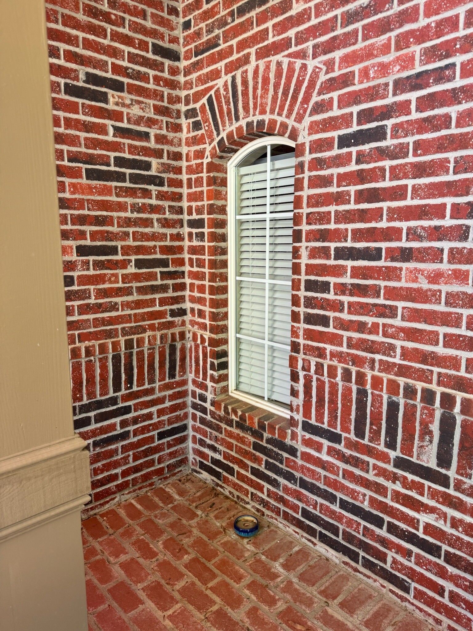 Brick wall corner with arched window, red and black bricks, white blinds, tan support column.
