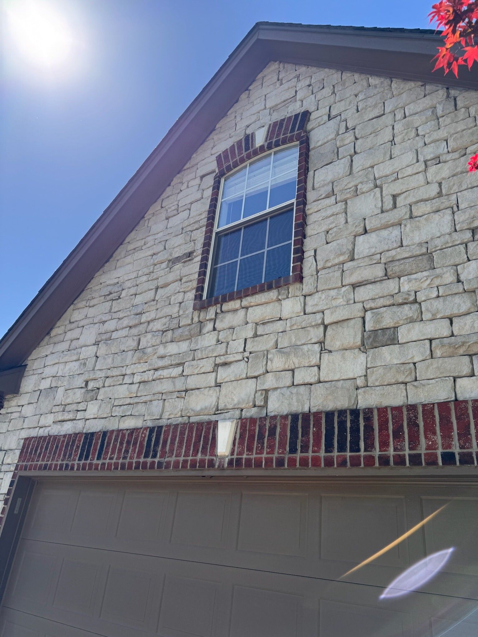 Stone brick house exterior with a window and a garage door, under a sunny sky.