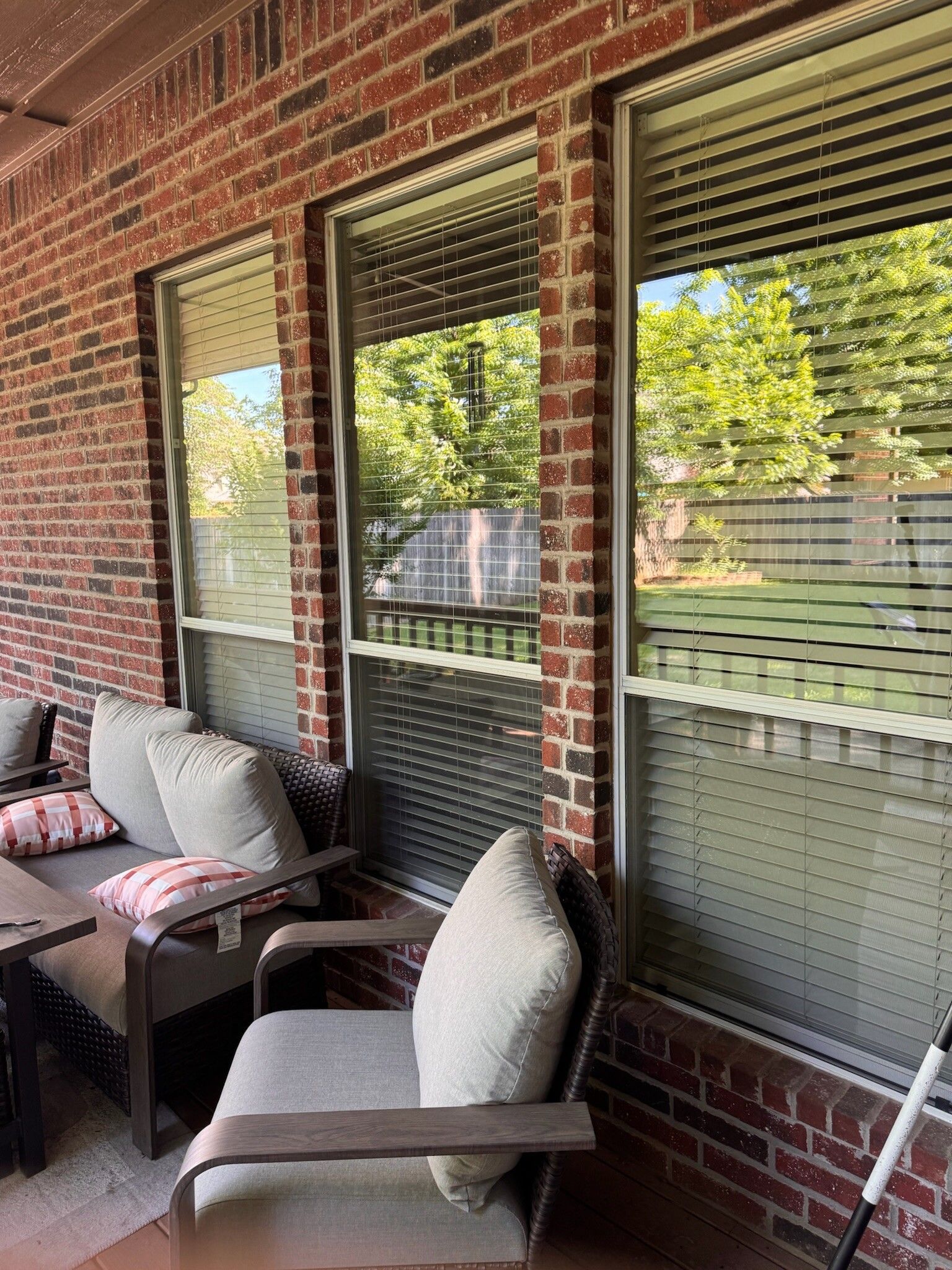 Outdoor seating area with brick wall, windows with blinds, and trees visible outside.