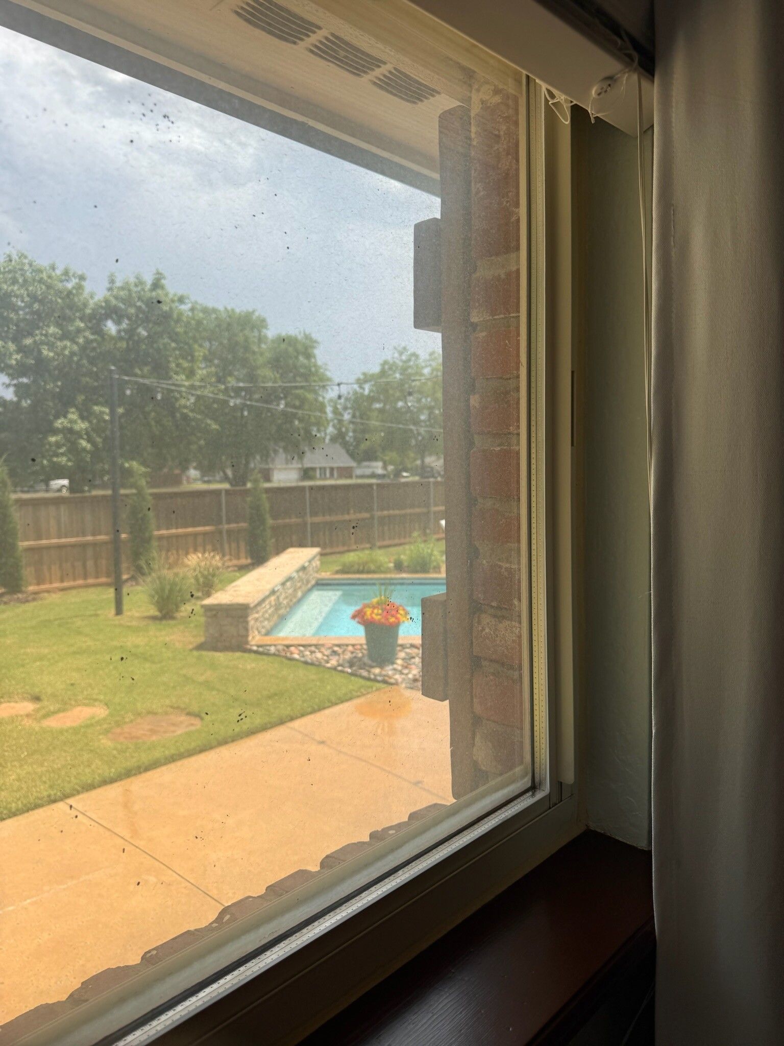 View of a backyard with a pool through a window, brick wall visible.