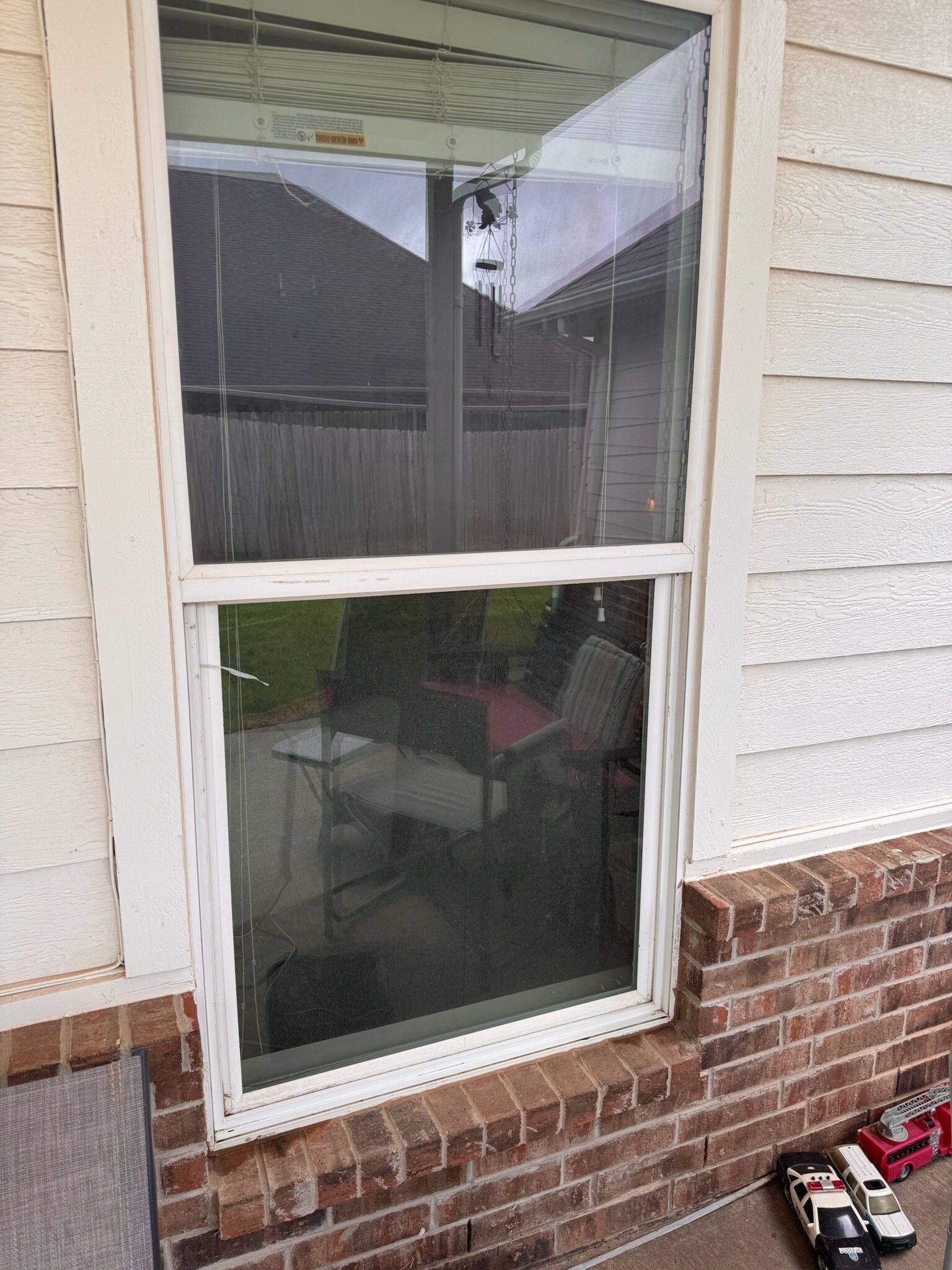 White-framed window in a brick and siding exterior wall. The window is closed with a screen.