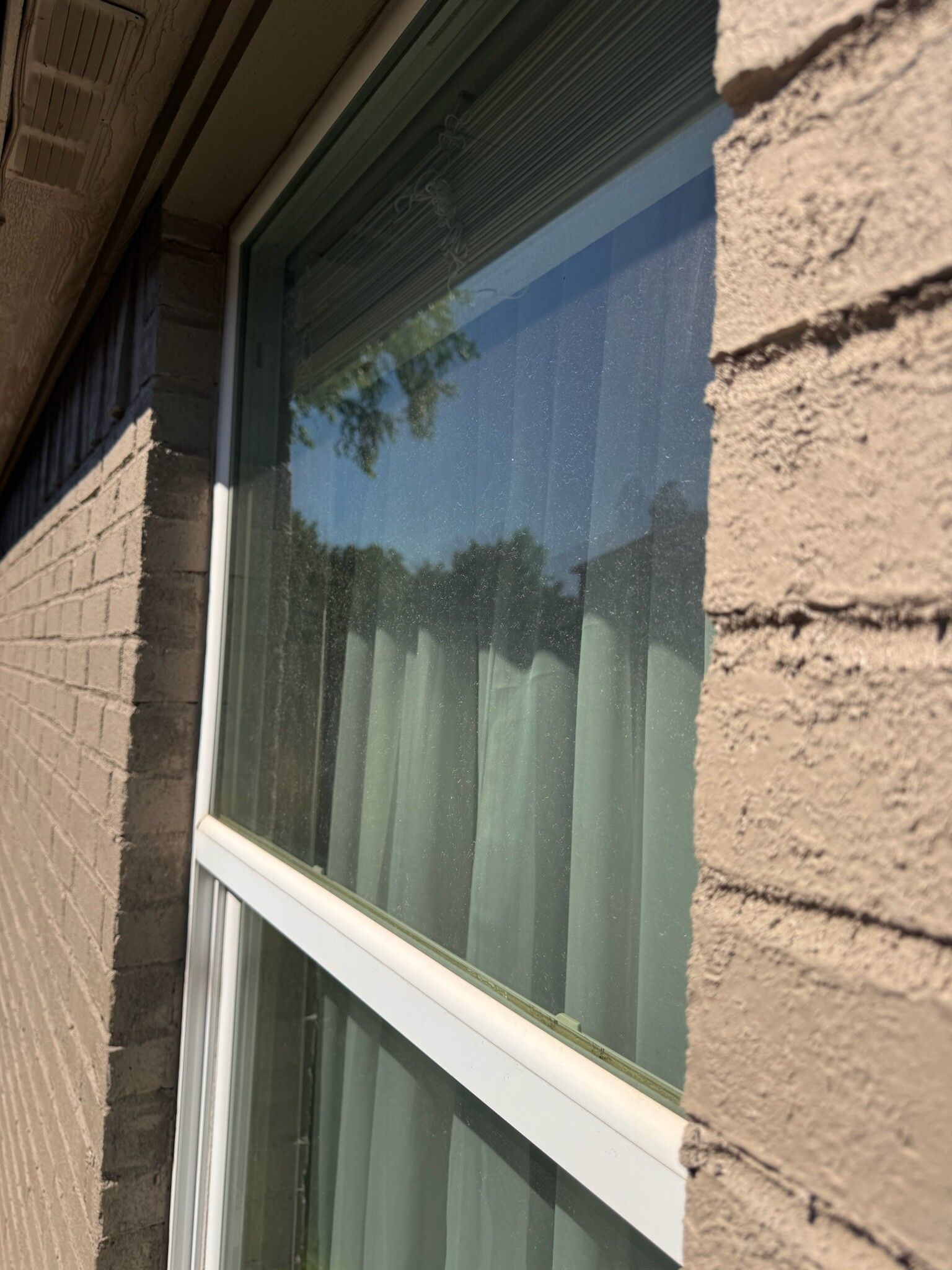 Exterior view of a window with white trim, set in a brick wall. Sunlight reflects on the glass.