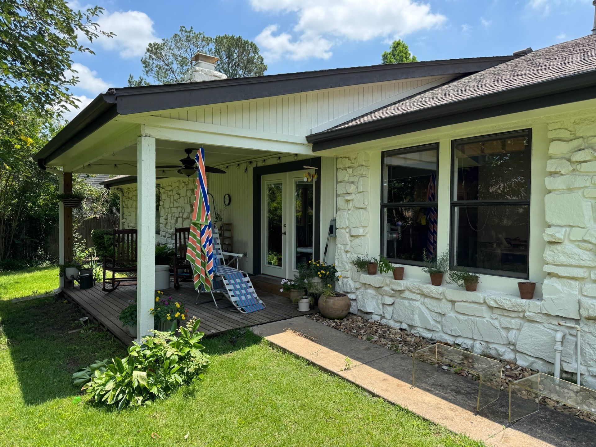 White stone house with a covered porch and brick pathway; green lawn and blue sky.