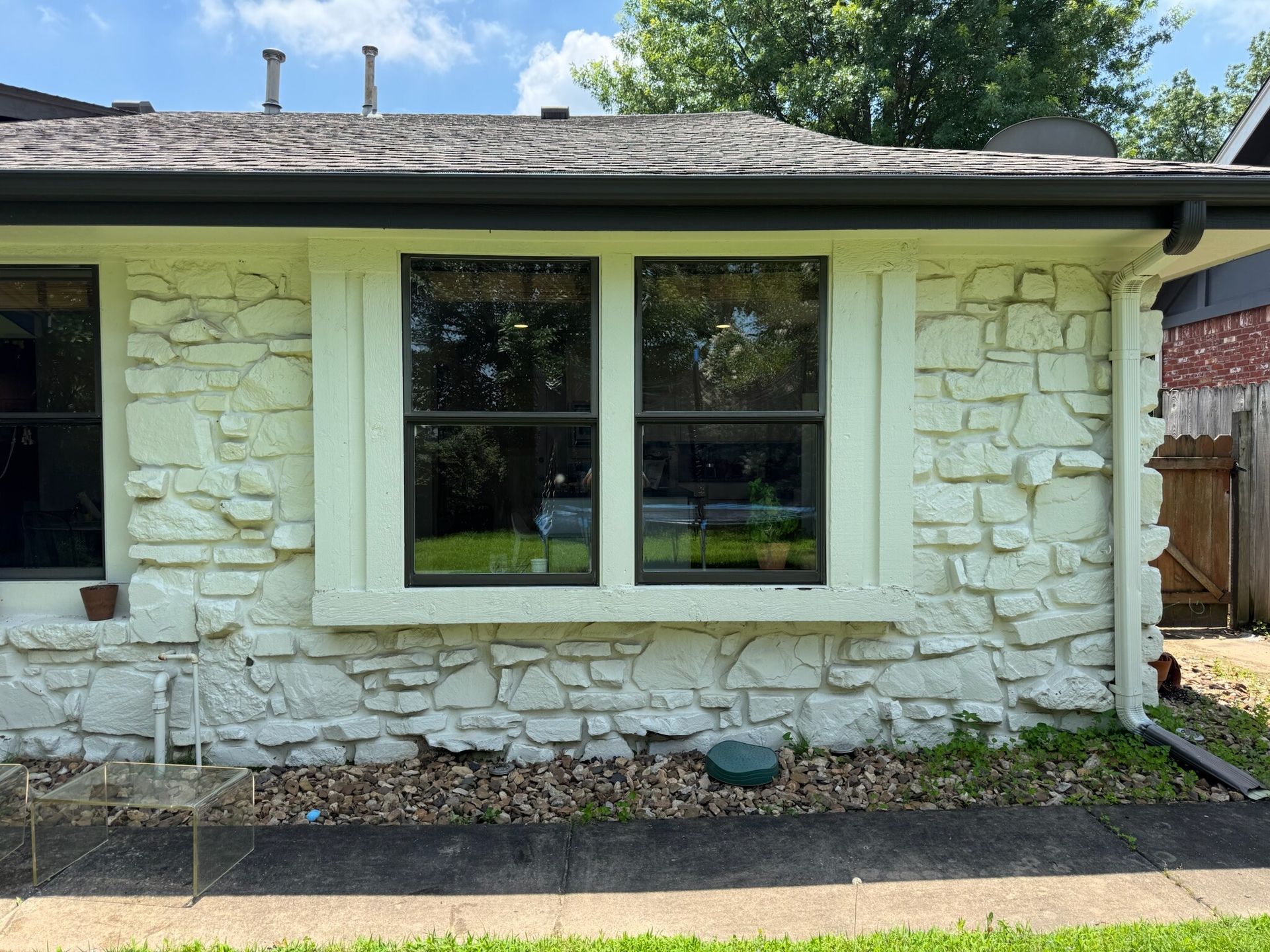 Exterior of a house with stone-like siding, a double window, and a dark roof under a bright sky.