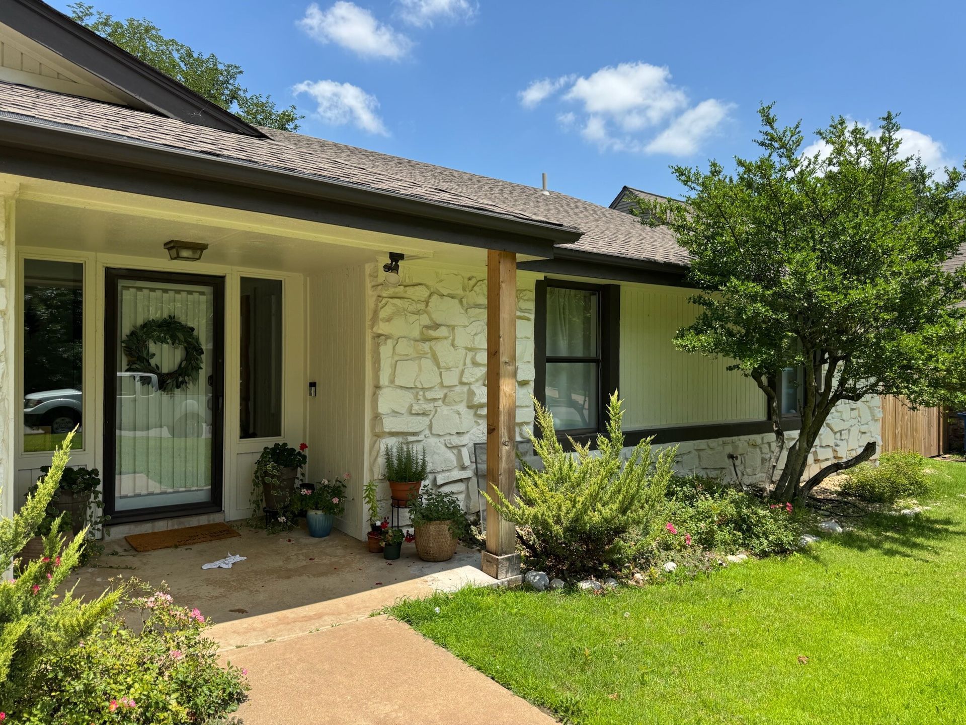 A house with white stone facade, a wreath on the door, and lush green lawn.
