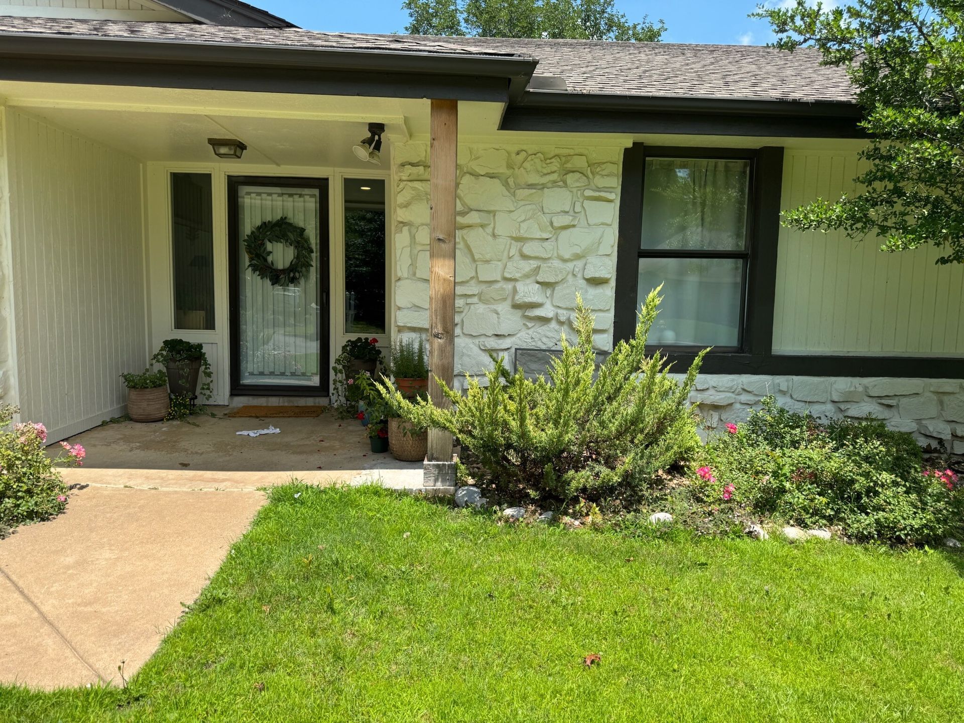 House exterior with white stone facade, black trim, front door with wreath, and green lawn.