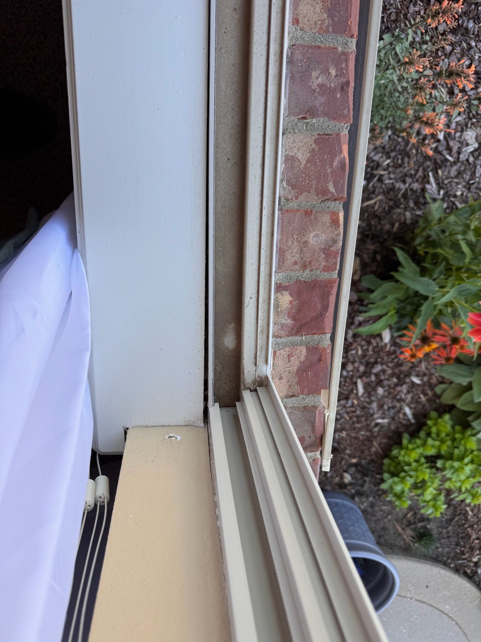Exterior window frame; white siding next to a brick wall.