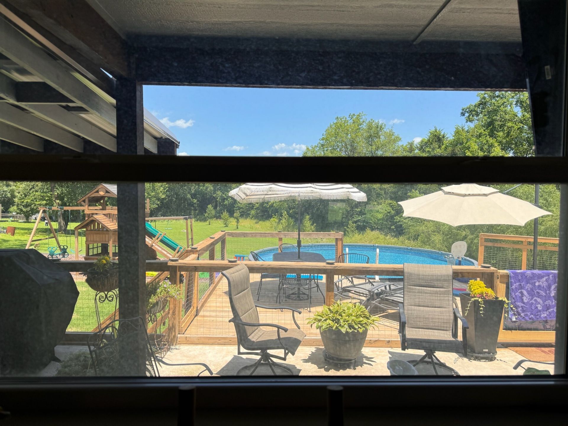 View of a backyard with a deck, pool, and trees, framed by a porch.