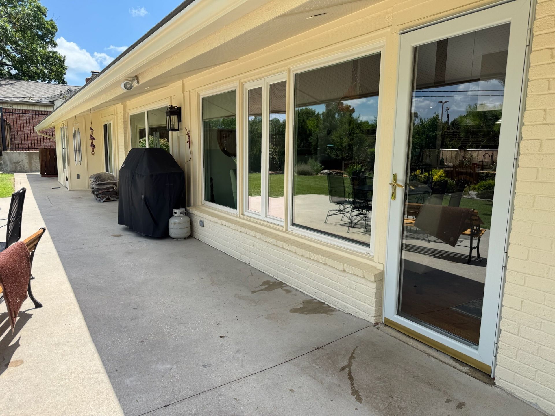 Back patio with sliding glass doors, concrete floor, and grill. Sunny day.