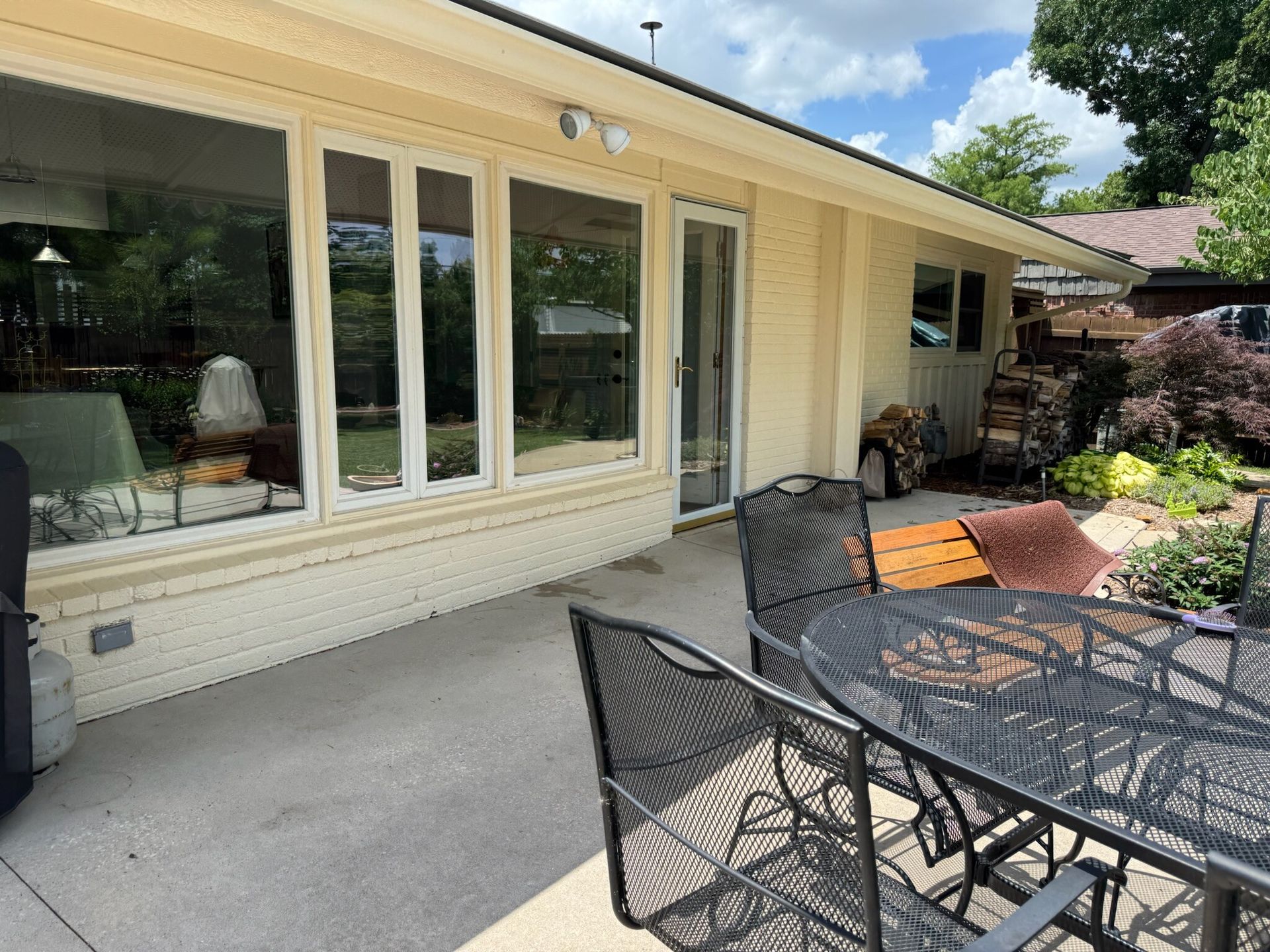 Patio with black metal furniture near a house with windows and a door, sunny day.