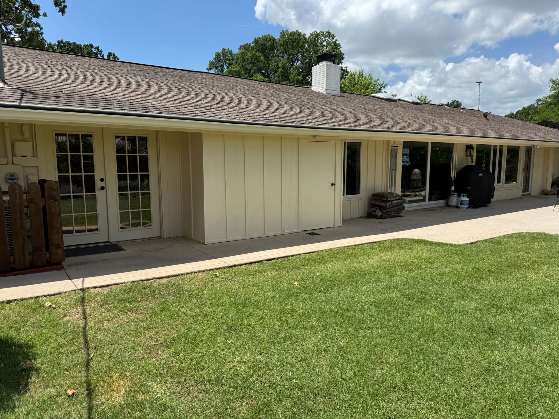 Beige house with brown roof, glass doors and windows, and a green lawn.