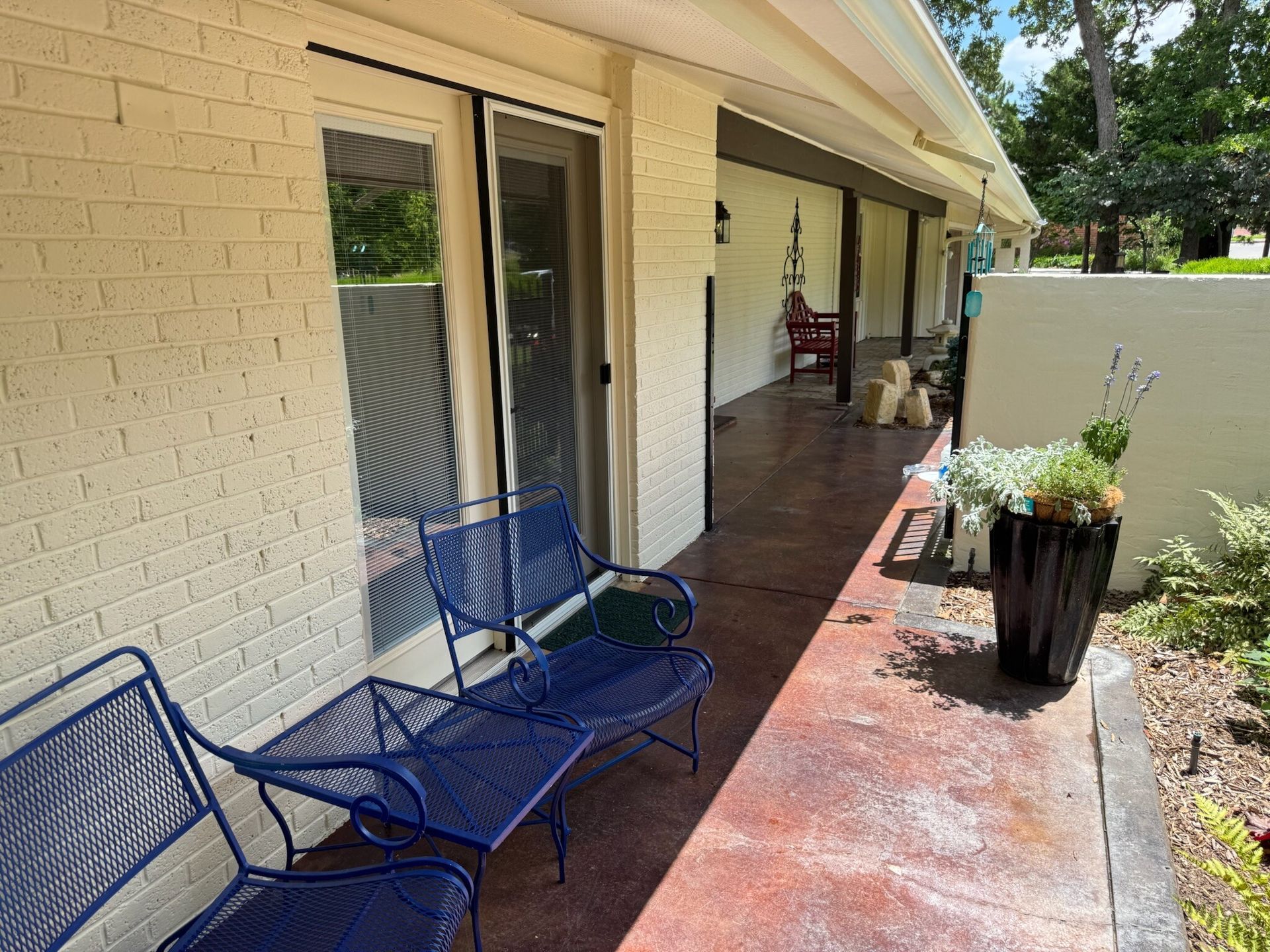 Blue patio chairs next to a brick wall with a sliding glass door and a red concrete walkway.