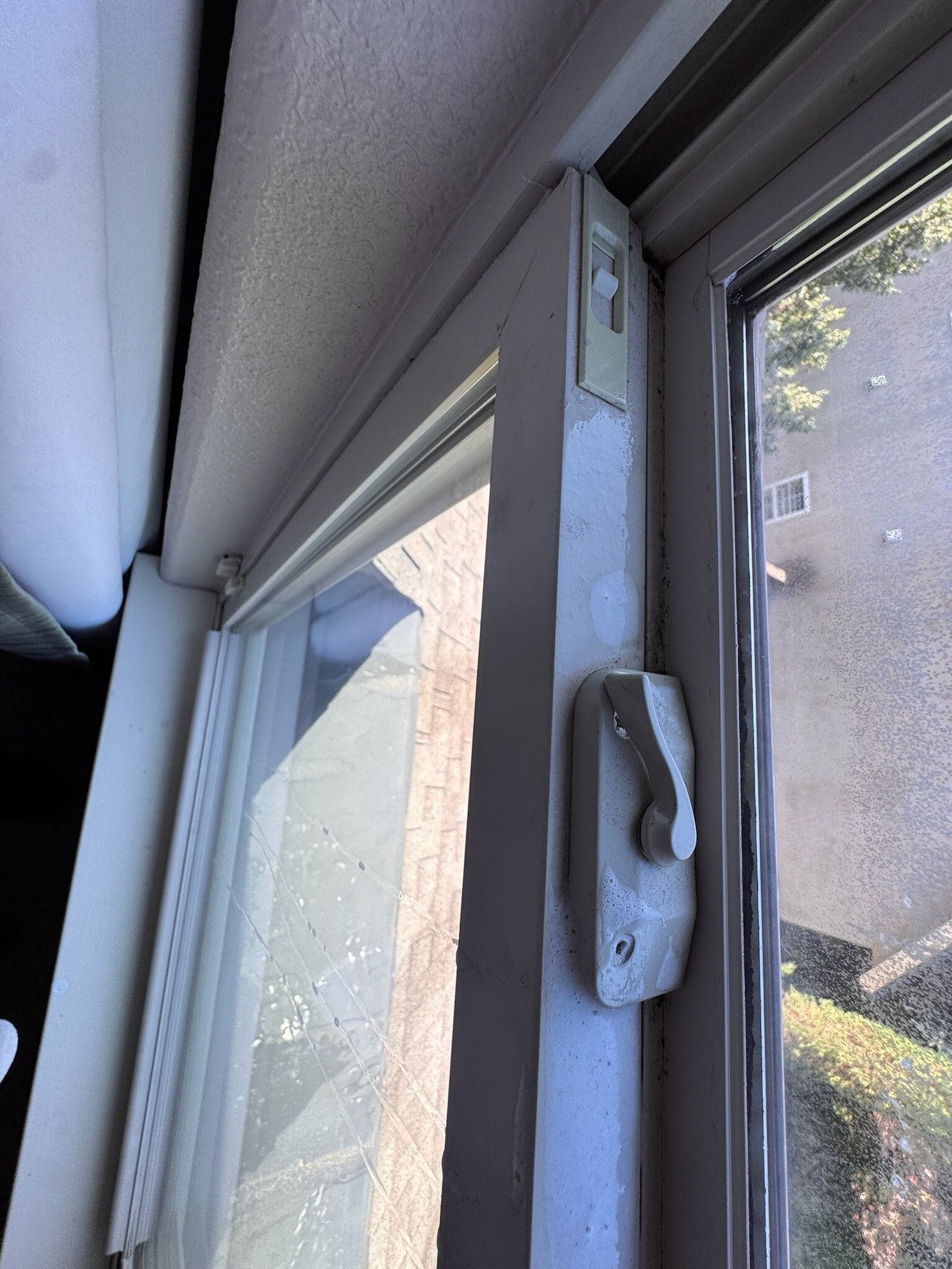 White window frame with a latch and lock, open, dirty glass, and a view of trees.