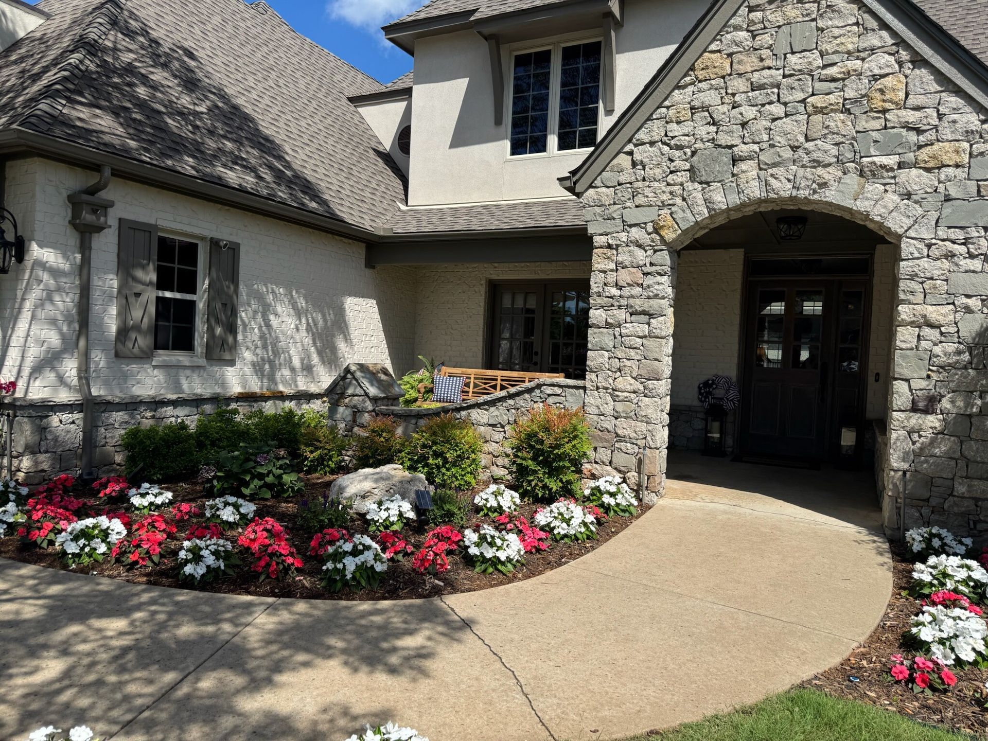 Stone and stucco house with arched entryway and pathway lined with red and white flowers.
