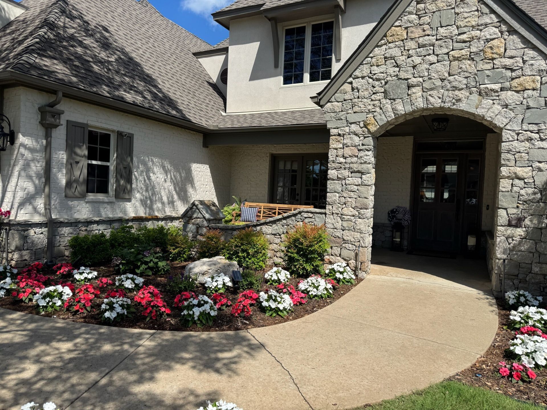 Stone house entrance with arched doorway and flower beds.