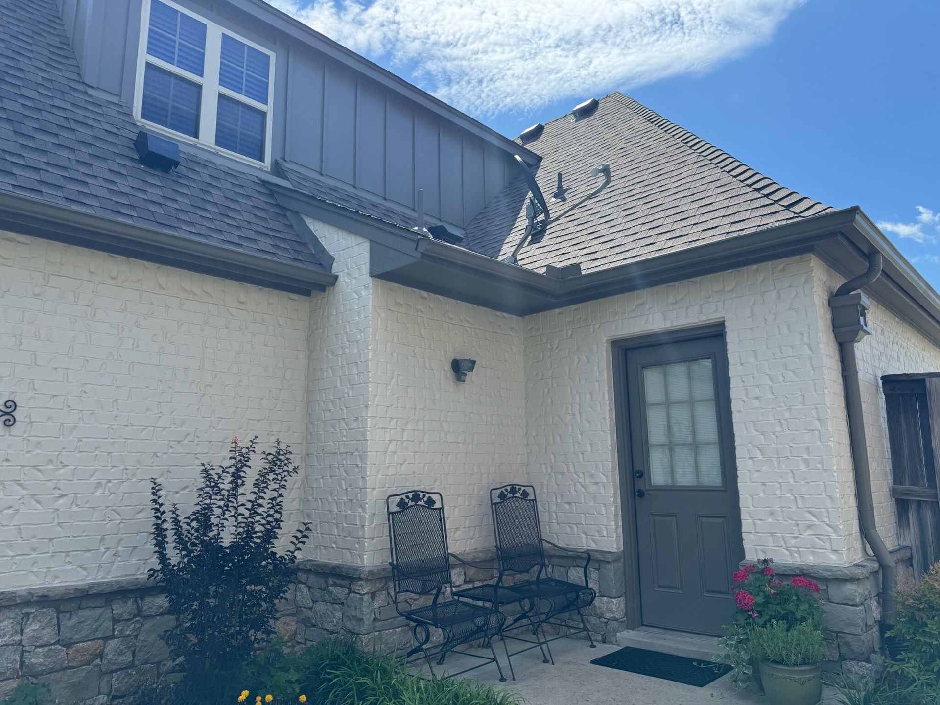 Exterior of a stucco house with a dark gray roof and door; seating area with two chairs.
