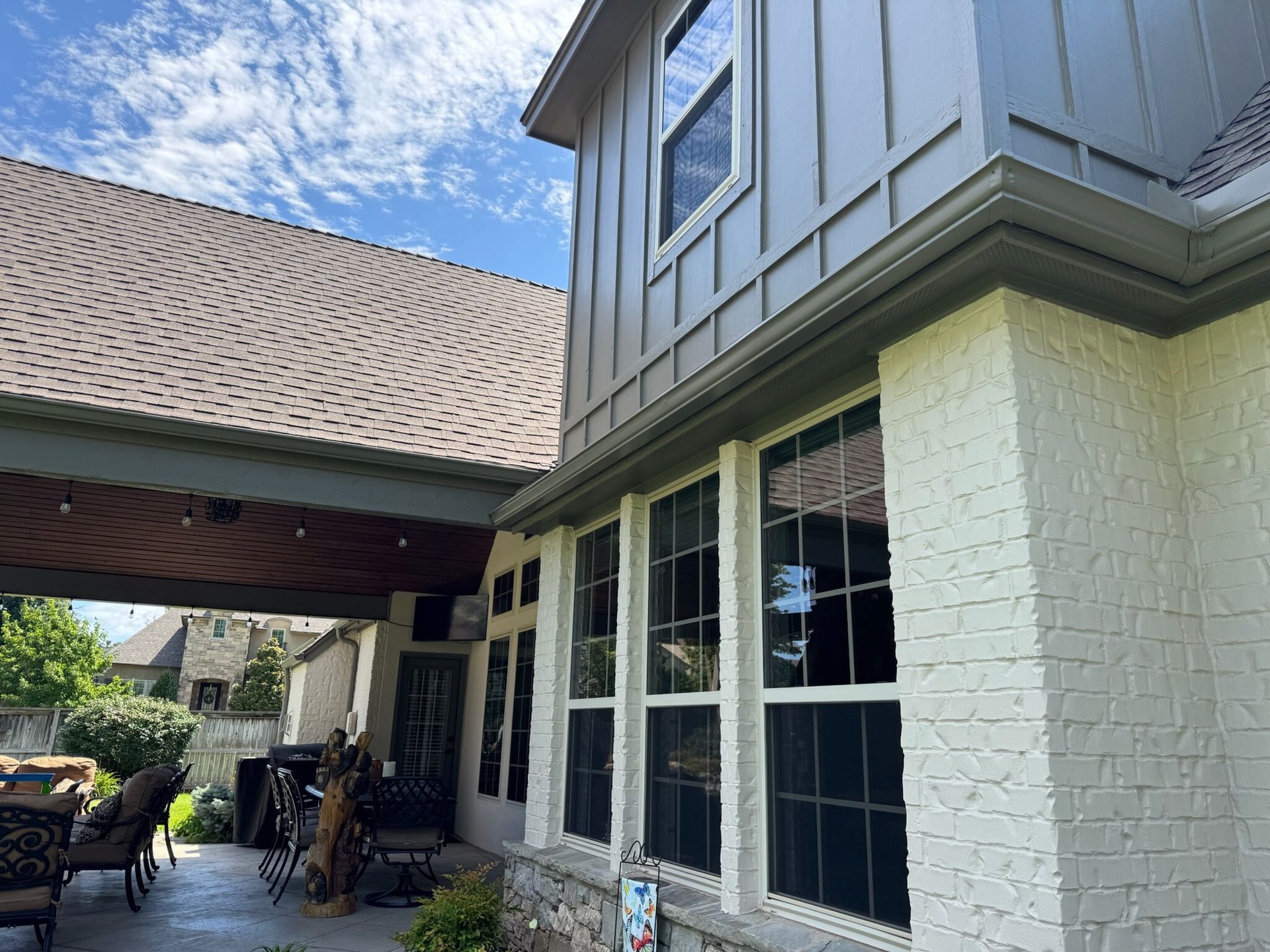 Exterior of a house with a covered patio. Gray siding, white brick, large windows, and a blue sky.