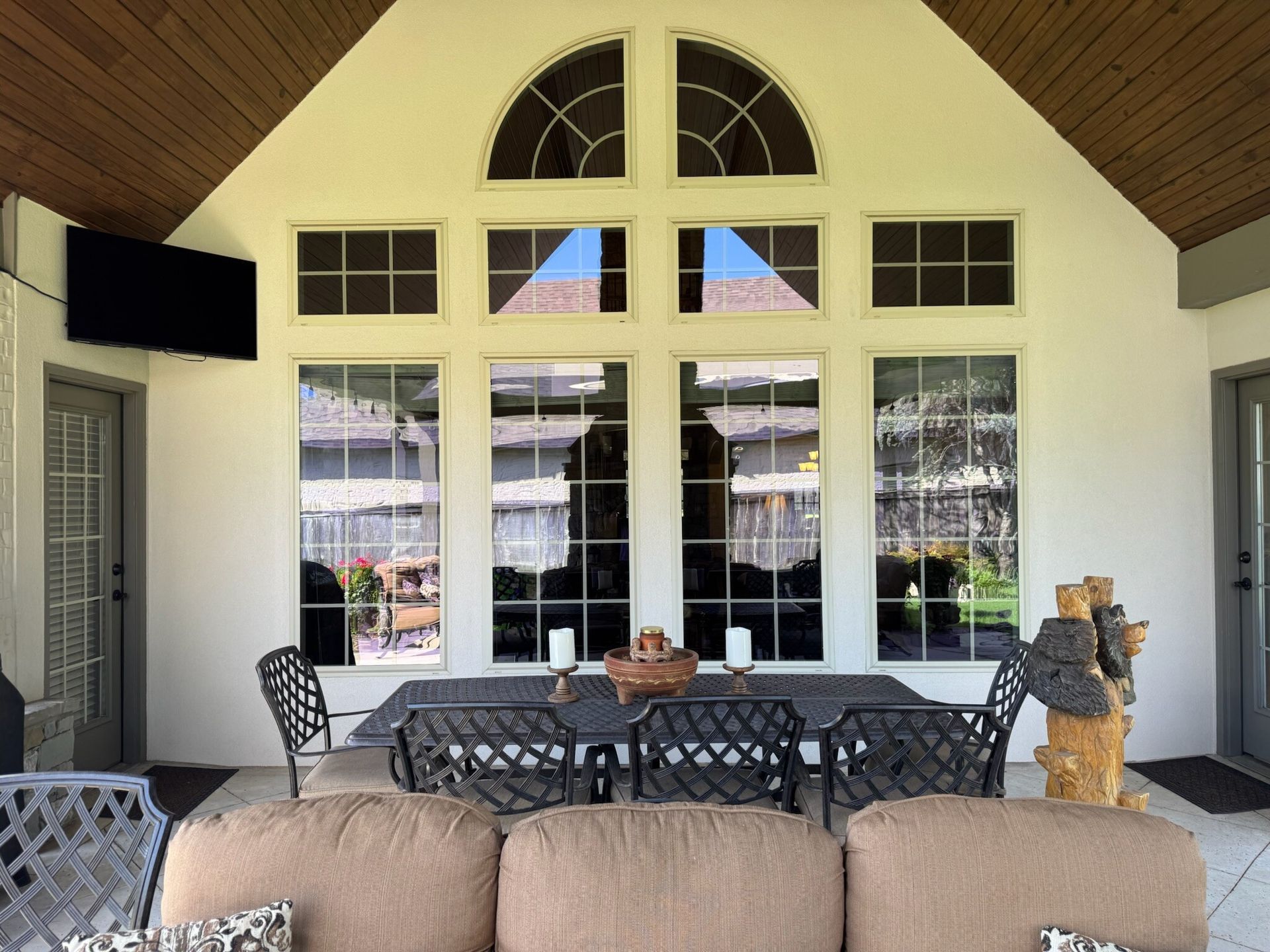Covered patio with large windows reflecting the outside. Outdoor furniture includes a dining table and sofa.