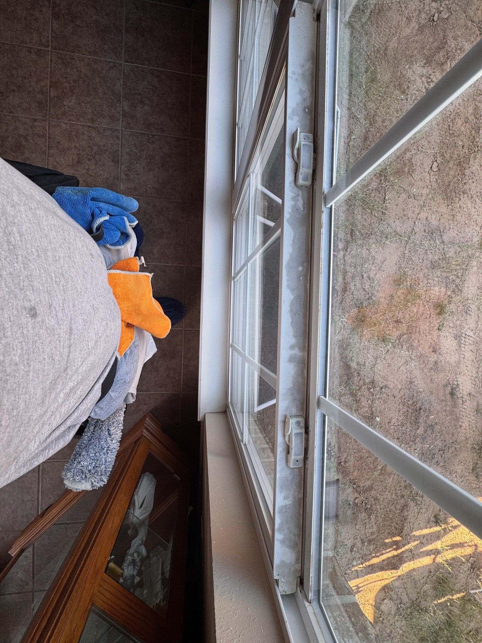 Window with white bars, next to a brown tiled floor, with a pile of towels and a brown framed object.