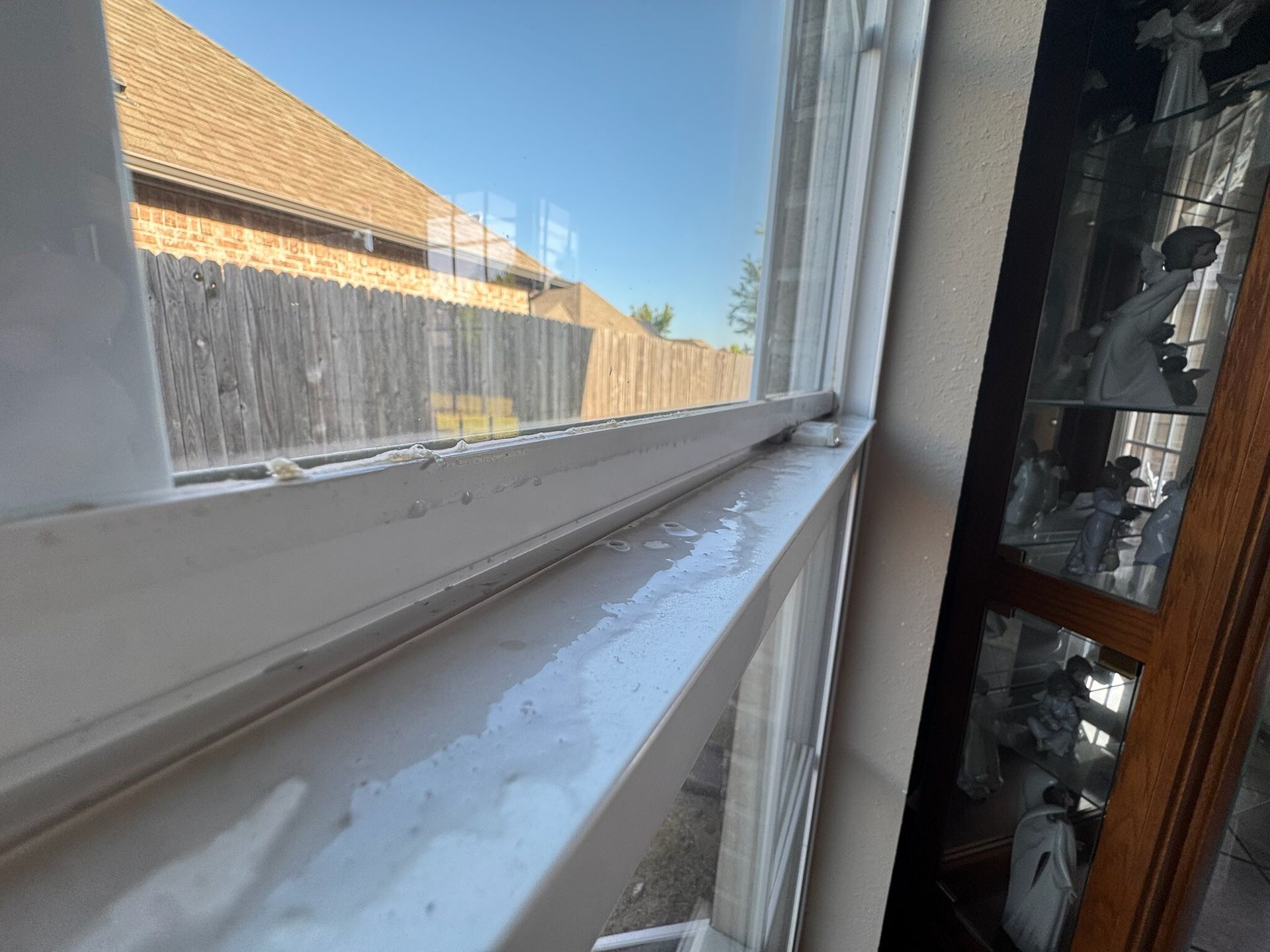 White window frame with condensation. View of wooden fence and sky outside.