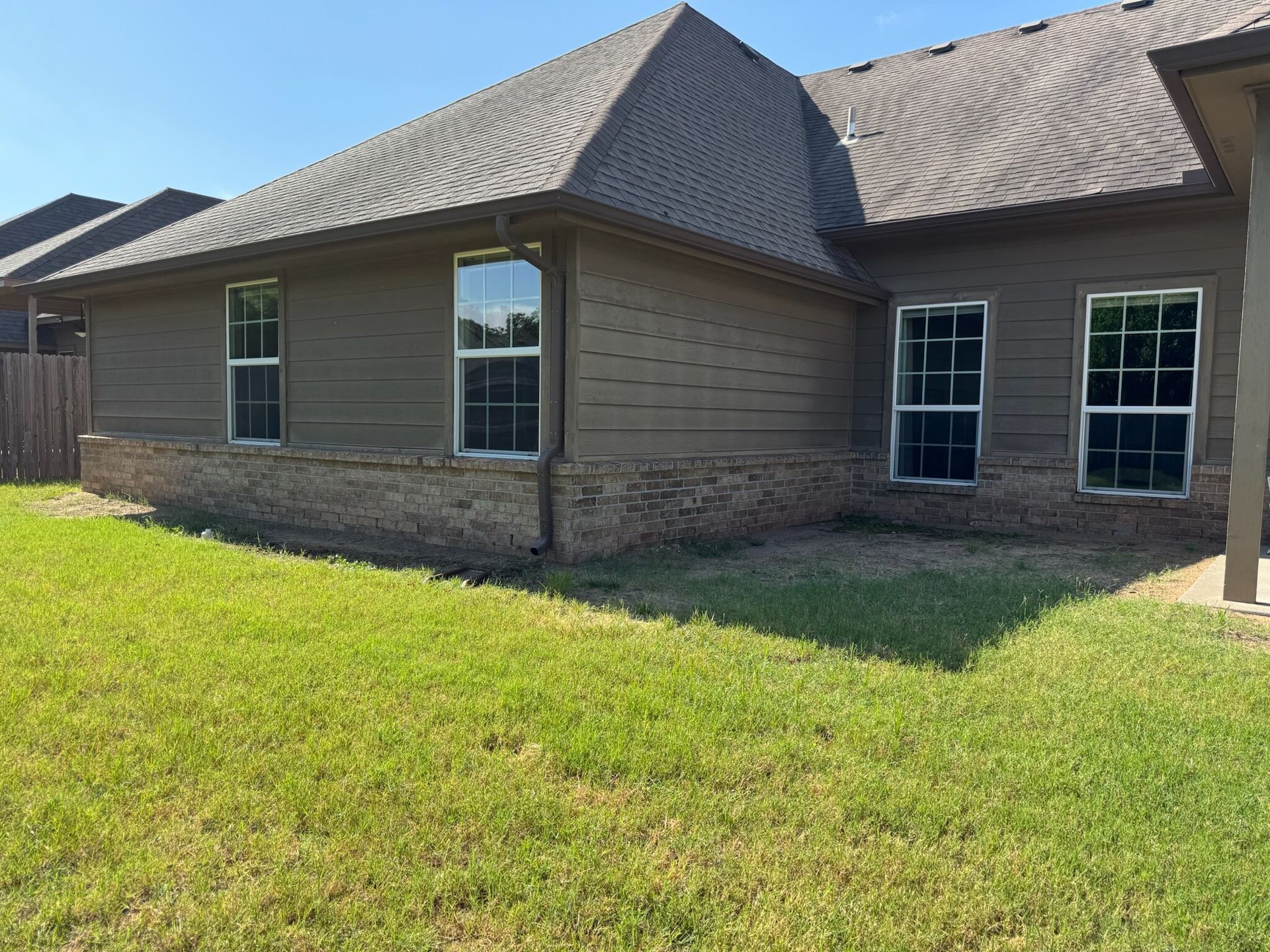 Side view of a house with a brown roof and siding. Several windows are visible. Green grass in foreground.