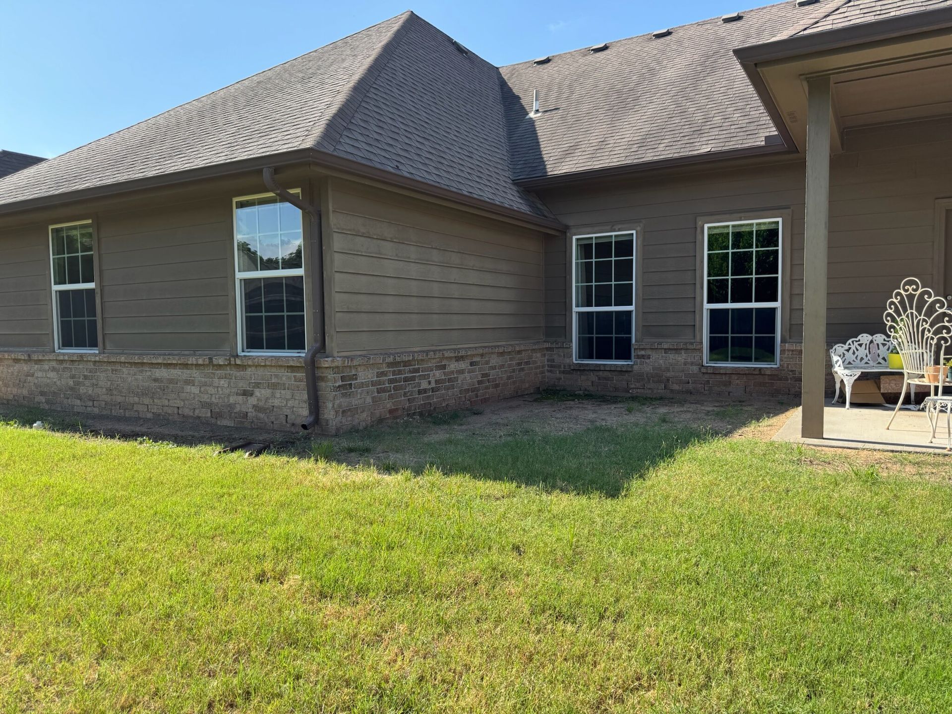 Exterior of a brown house with multiple windows and a grass lawn. A covered patio is on the right.