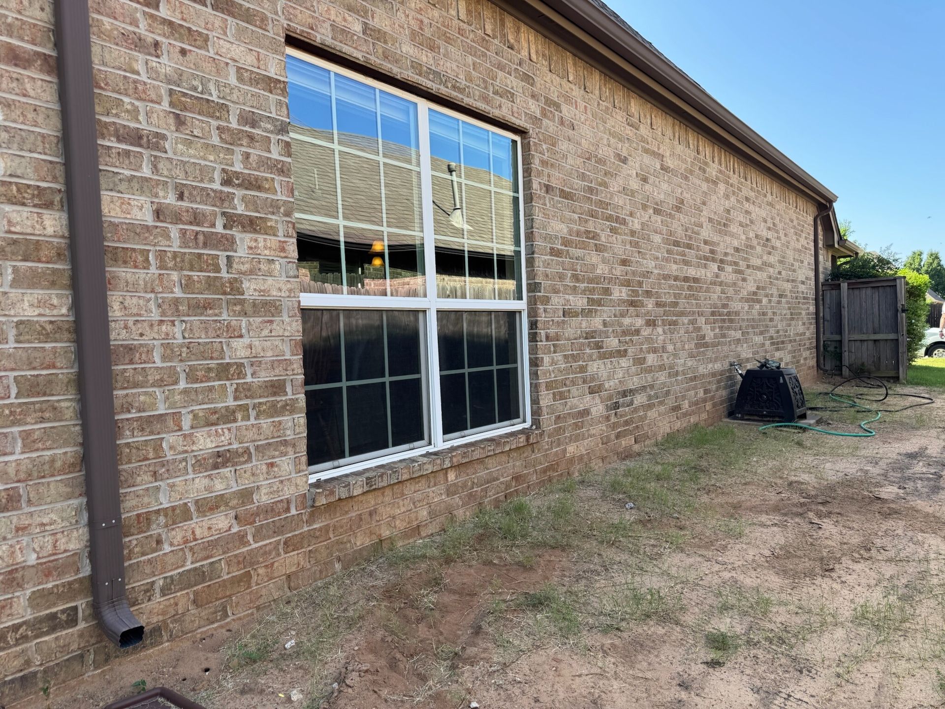 Brick building exterior with window, gutter, and overgrown yard.