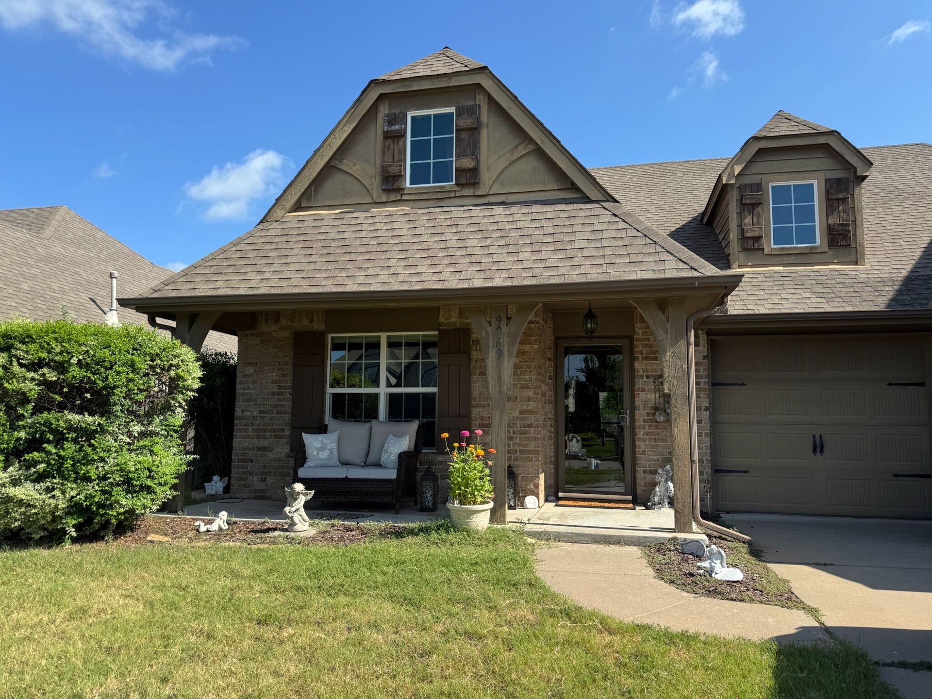 A tan brick house with a brown roof and a small porch with a white bench. The sky is blue.